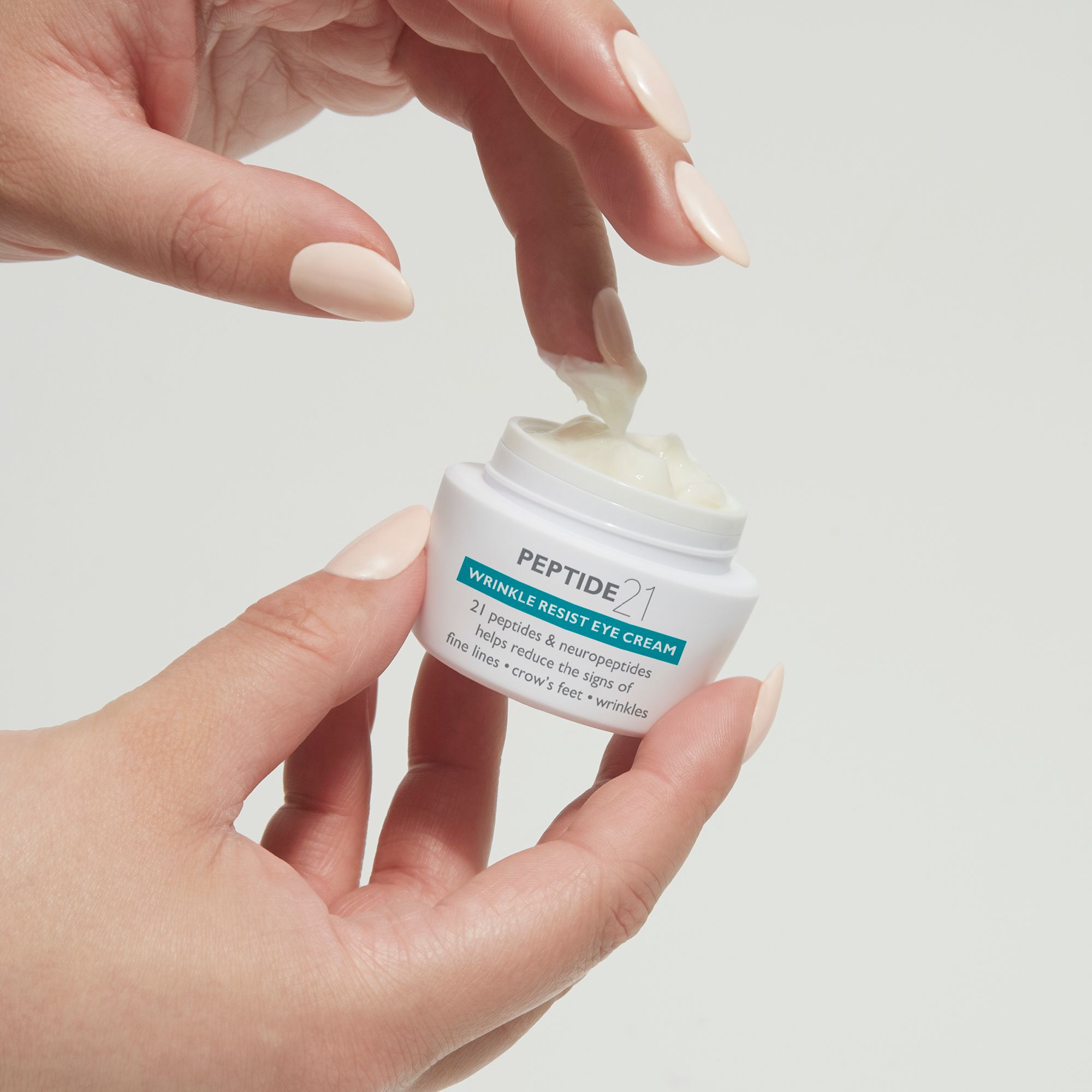 Mani che tengono Peter Thomas Roth Peptide 21® Wrinkle Resist Eye Cream. Crema prelevata.