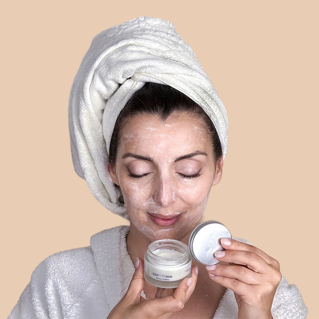 Donna con asciugamano in testa, crema sul viso, tiene vasetto.
