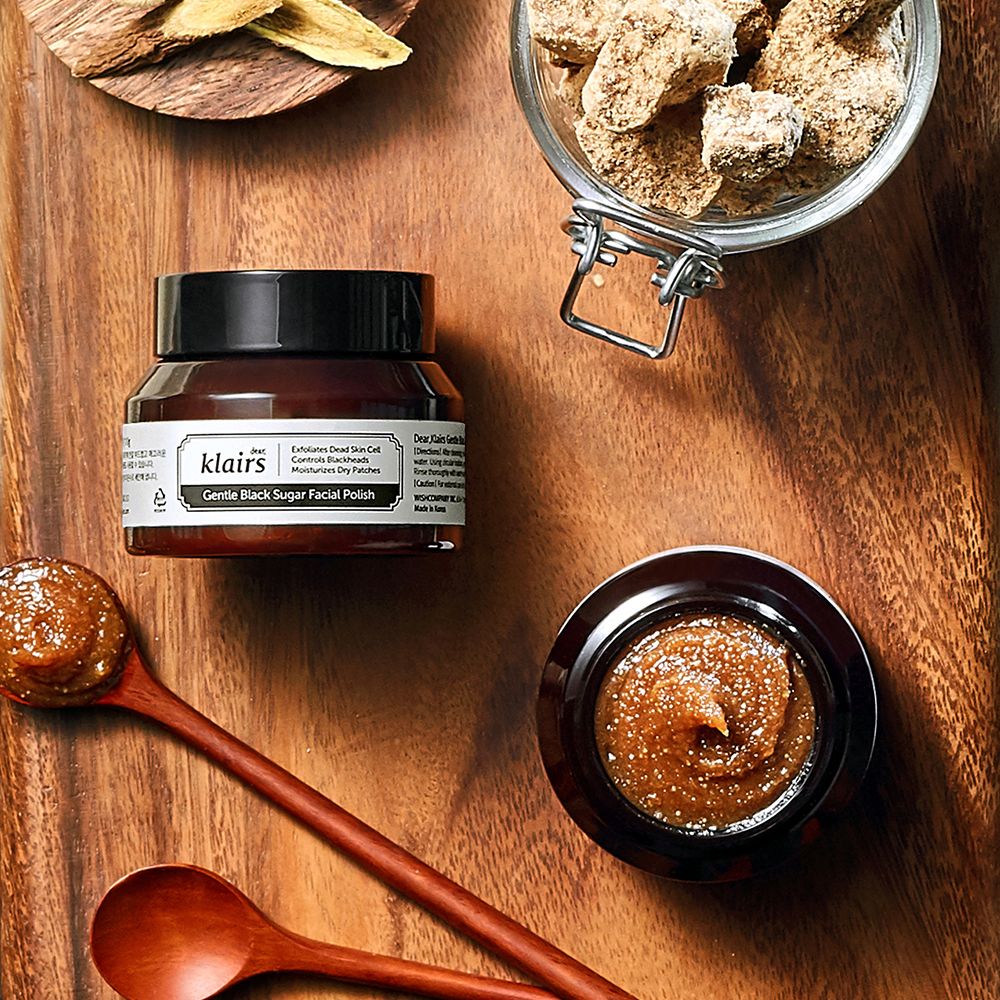 Klairs Gentle Black Sugar Facial Polish su un tavolo di legno con ingredienti come zucchero di canna.