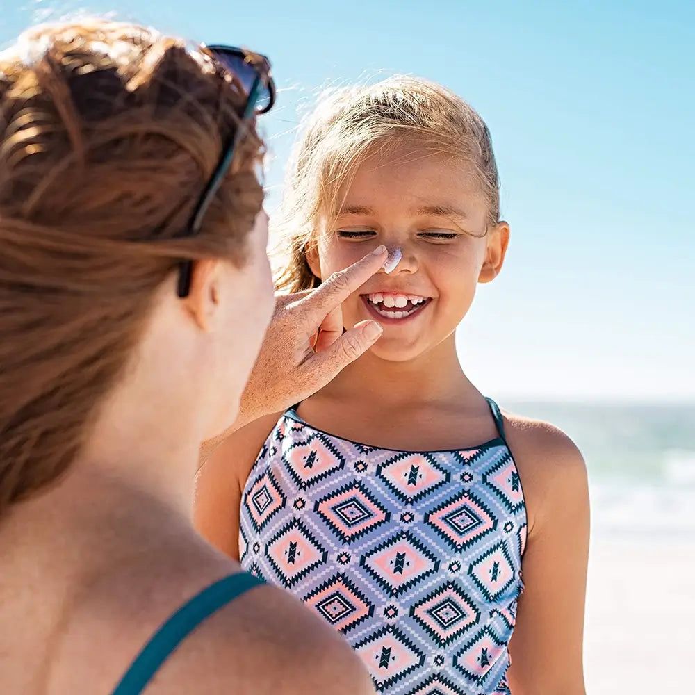 Una madre applica la protezione solare sul naso della figlia. La bambina indossa un costume da bagno in spiaggia.