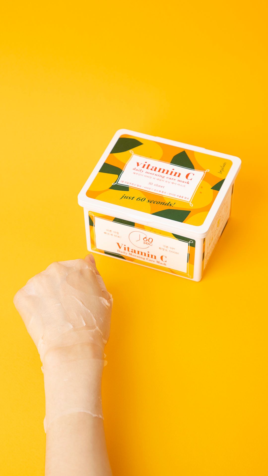 Contenitore di maschere alla vitamina C. Mano con maschera. Sfondo giallo. Scritta: Vitamin C Daily Morning Care Mask.