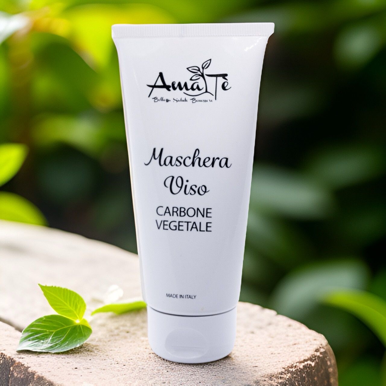 Tubo bianco Amatè Maschera Viso Carbone Vegetale su sfondo verde. Fogliame.