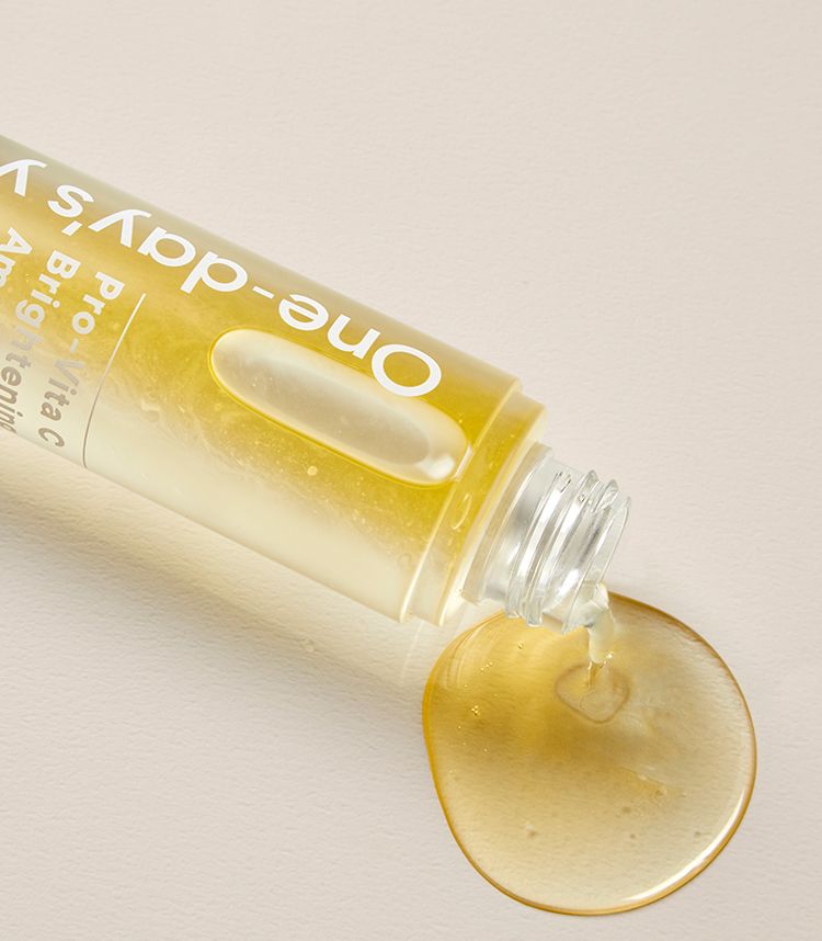 Un flacone trasparente con siero giallo che cola su una superficie. Etichetta: 'One-day's, Pro-Vita C, Brightening'.