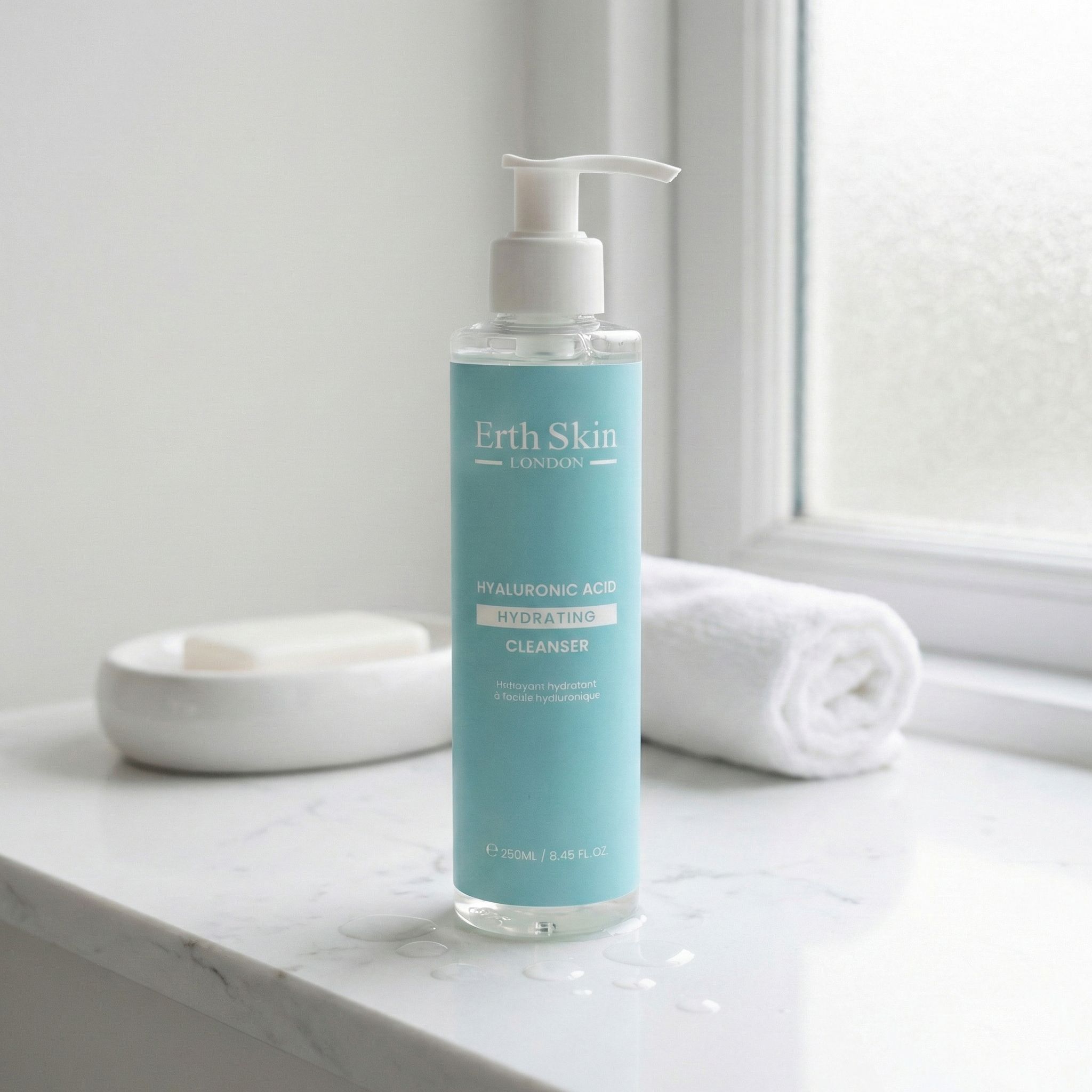 Detergente per la pelle con pompa su una superficie di marmo. Accanto a un asciugamano e un portasapone. Scritta: Erth Skin London, Hyaluronic Acid.