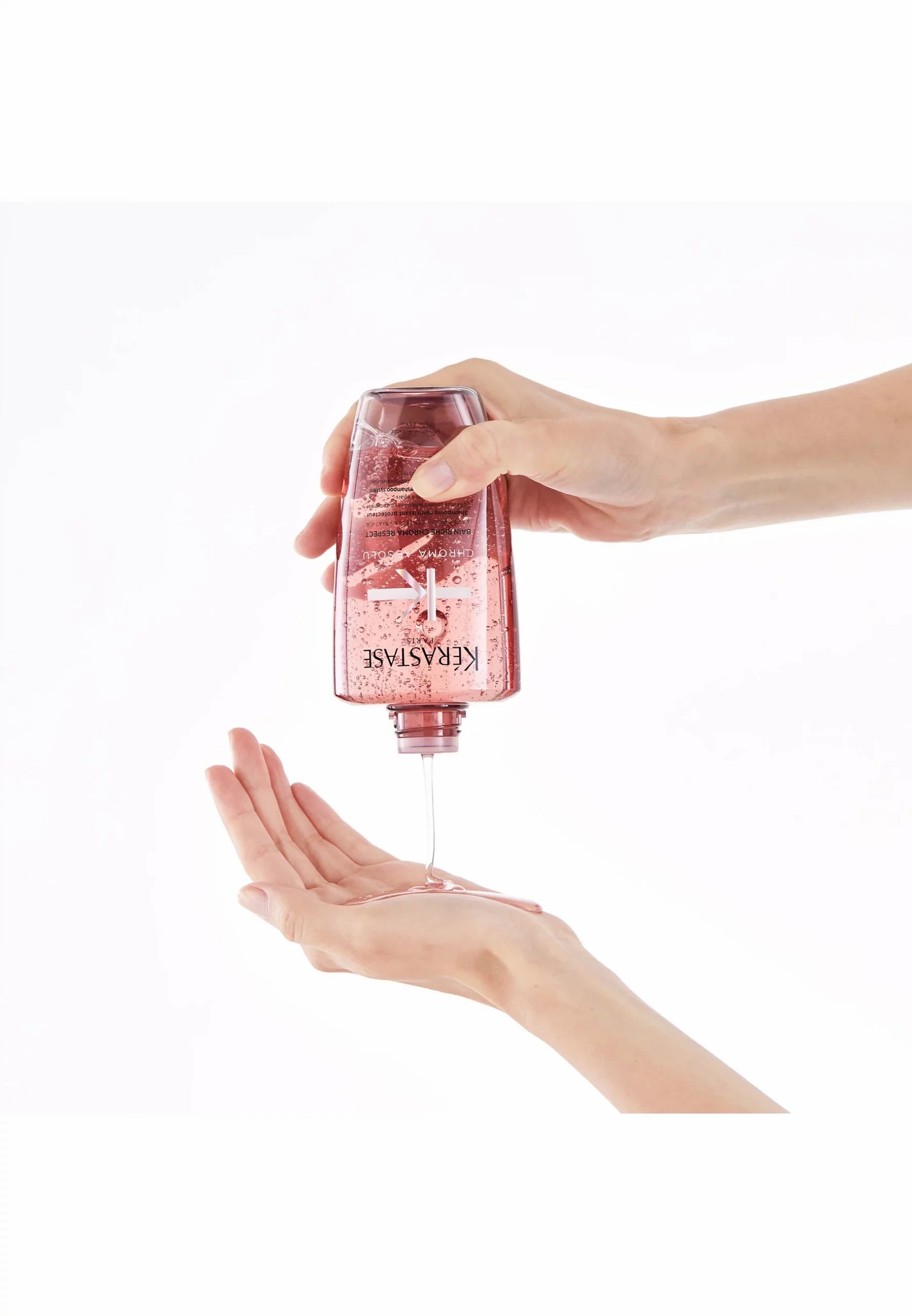 Mani che tengono un flacone di shampoo rosa, lasciando cadere liquido nel palmo.