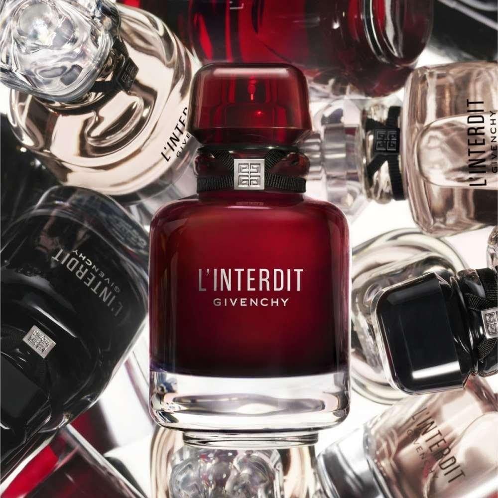 Flacone rosso circondato da altri flaconi. Scritta: L'Interdit Givenchy. Diversi flaconi sullo sfondo.