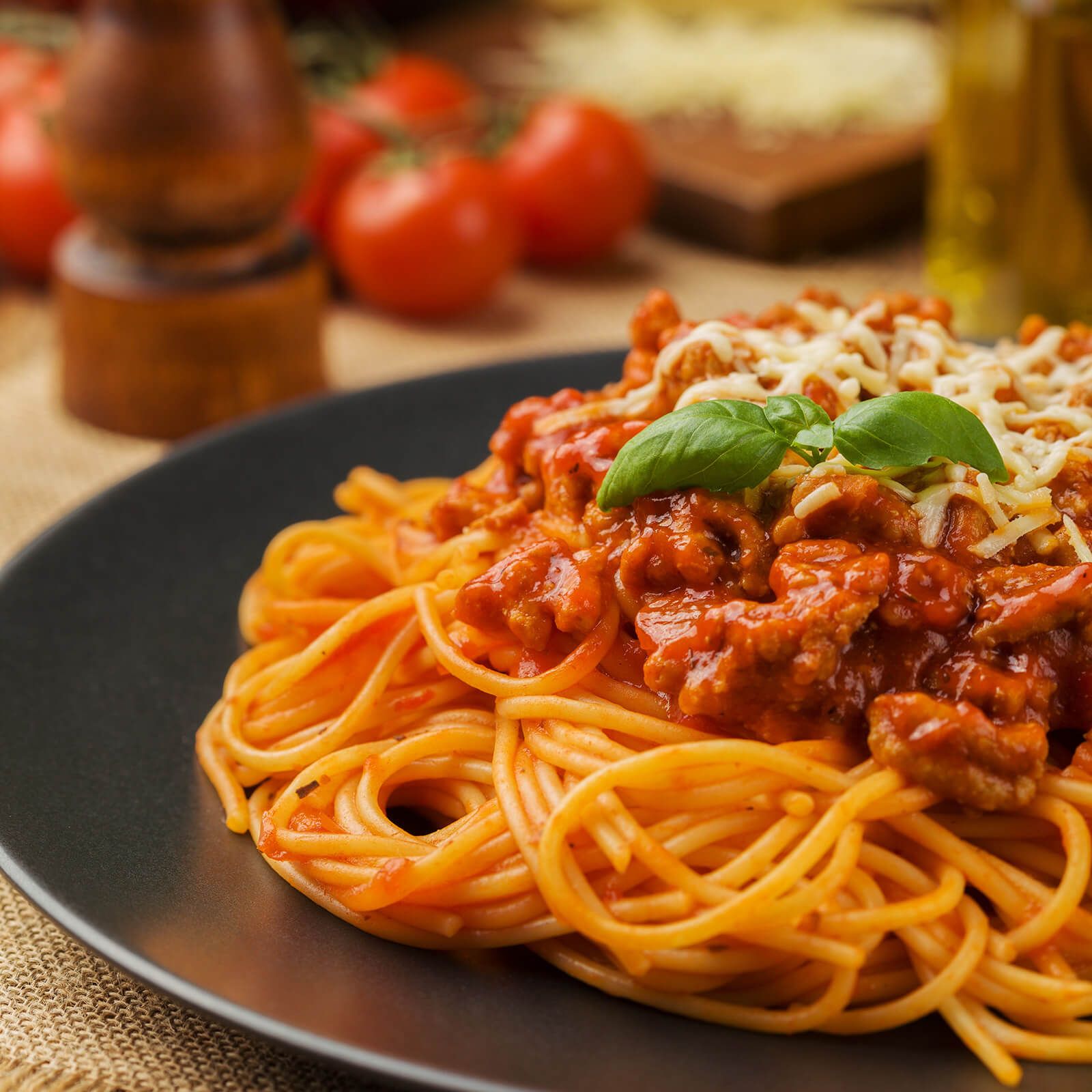 Piatto di spaghetti con salsa di pomodoro, carne e formaggio. Pomodori sullo sfondo.