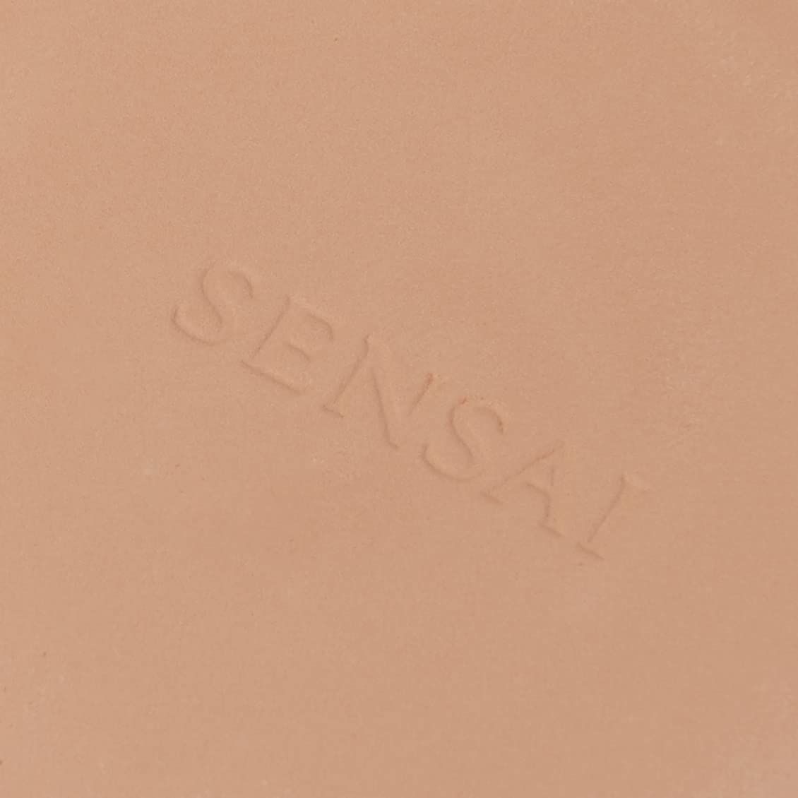 Primo piano di un compatto di polvere beige chiaro. La scritta Sensai è in rilievo.