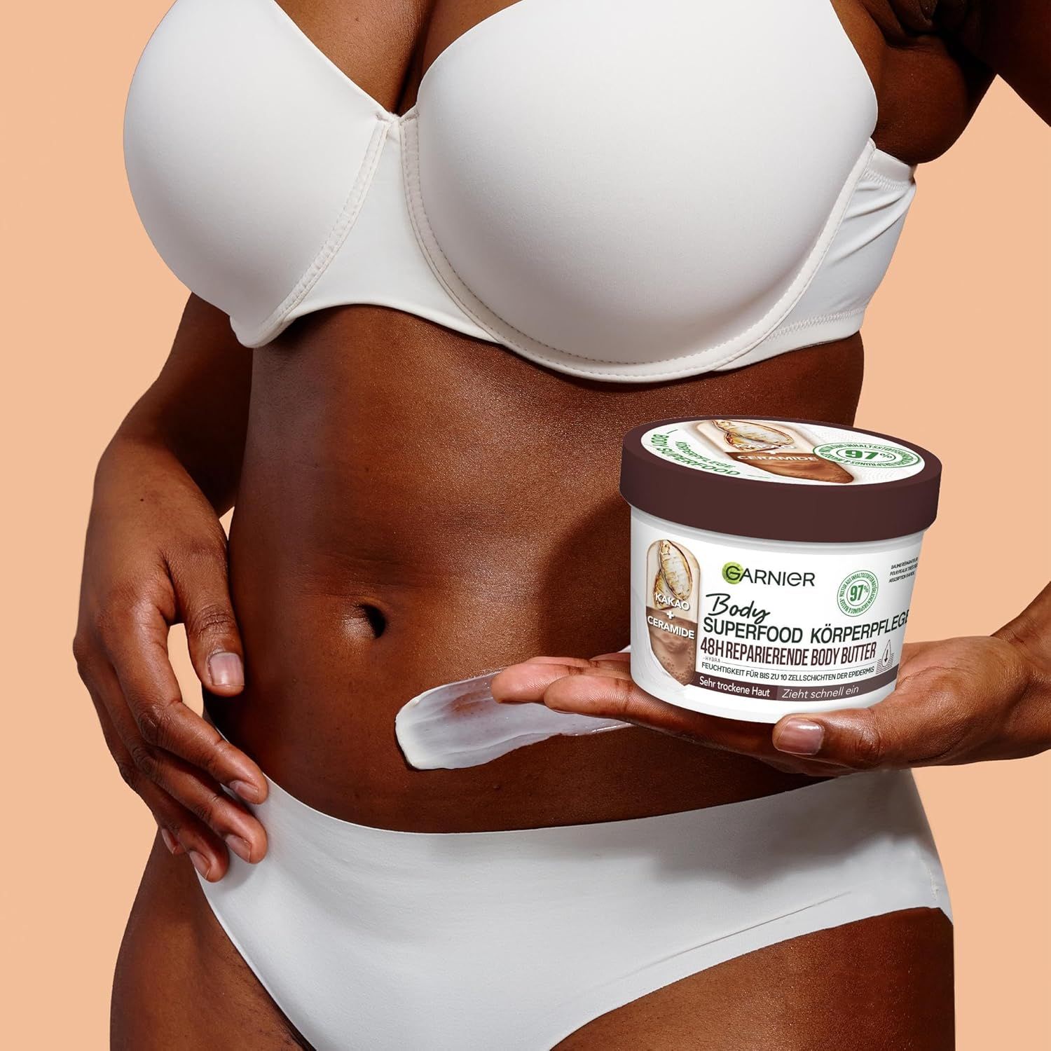 Persona che tiene un barattolo di burro corpo Garnier Body Superfood al burro di cacao. Crema sulla pancia. Testo: 48h riparatore.