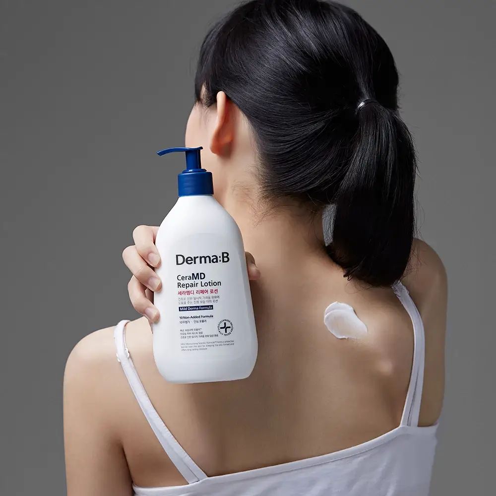 Donna tiene in mano flacone bianco con erogatore blu. Scritta: Derma:B CeraMD Repair Lotion. Crema sulla schiena.