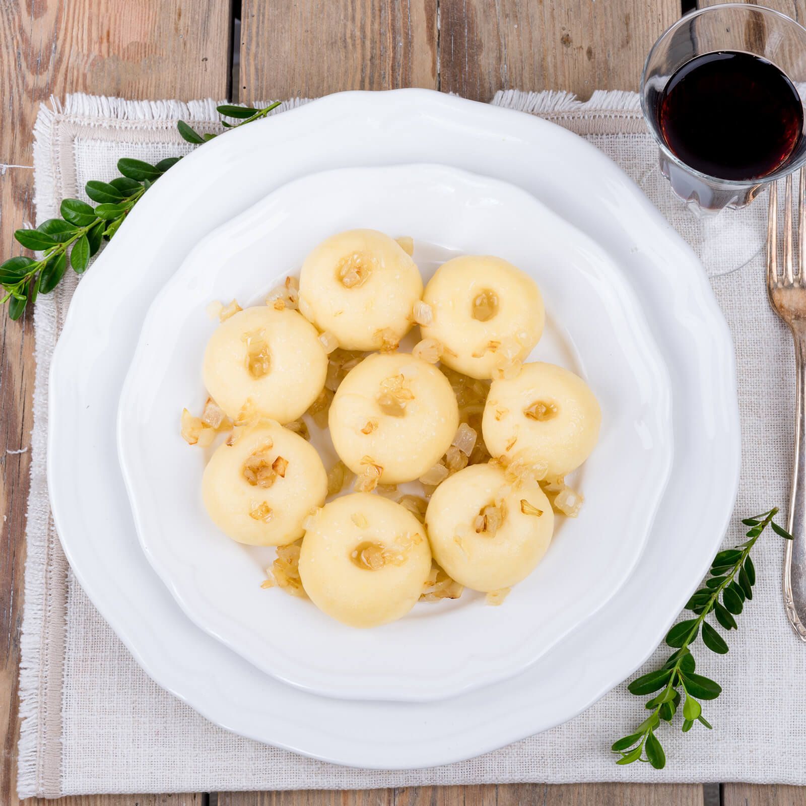 Piatto di gnocchi, serviti su un tavolo. Guarniti con cipolle. Decorazione con verde.