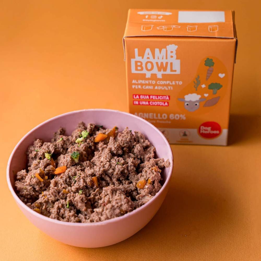 Ciotola rosa con cibo. Accanto, una scatola Dog Heroes Lamb Bowl. Scritto: Agnello 60%, verdure. Cibo con verdure.