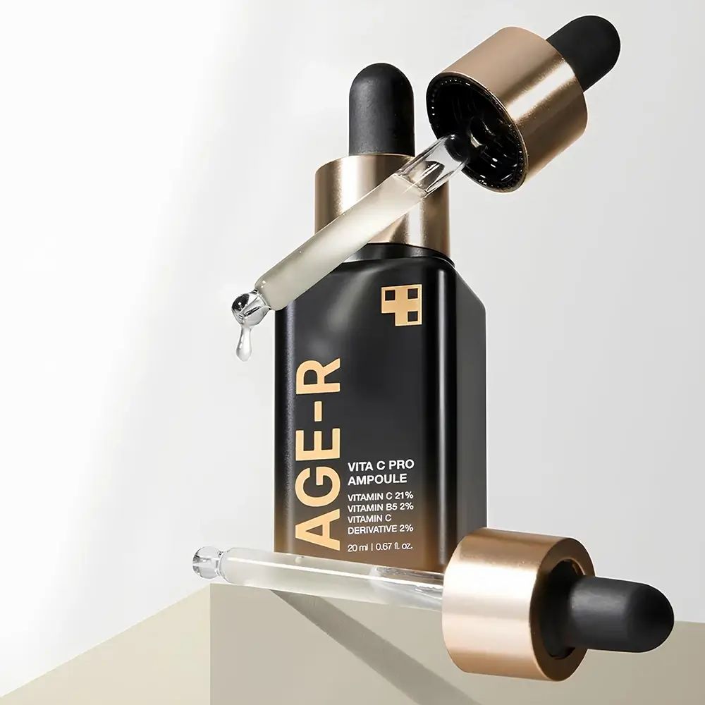 Flacone nero, scritte dorate. Due pipette. Forma quadrata. Goccia di liquido.