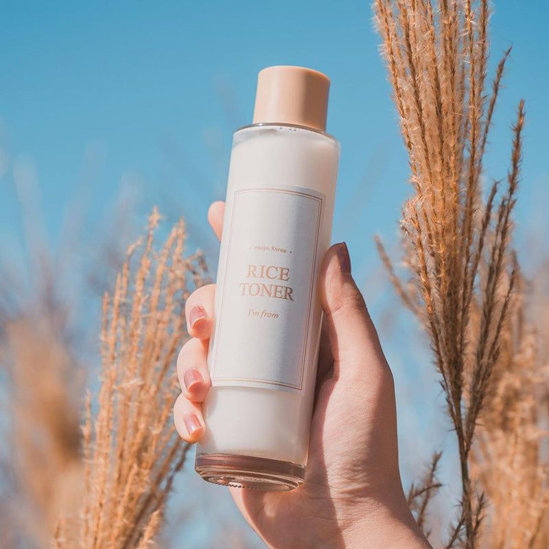 Tonico viso al riso in una mano. Bottiglia trasparente con etichetta, davanti a erbe.