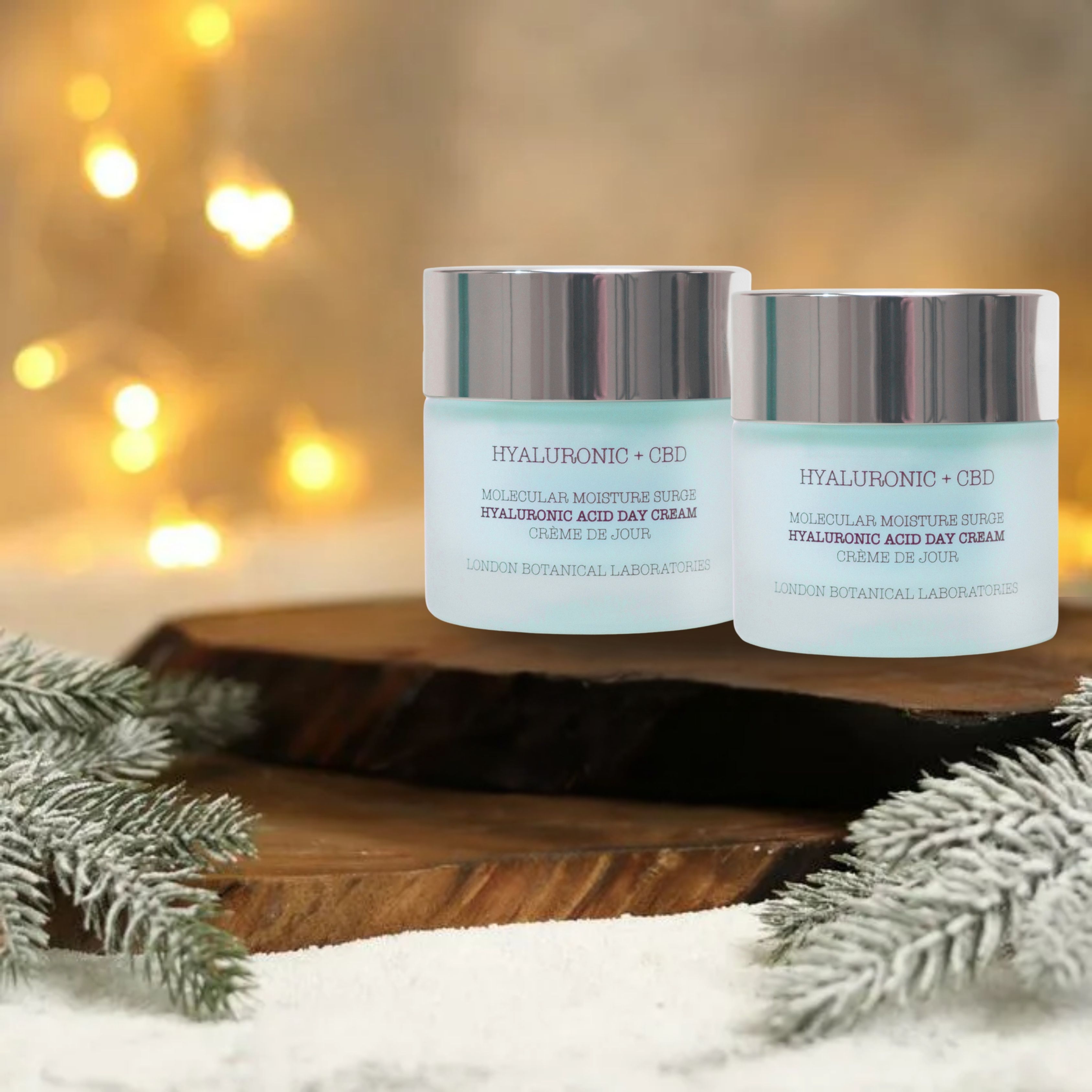 Due vasetti di crema giorno su una tavola di legno, con decorazioni natalizie. Scritta: Hyaluronic + CBD, Molecular Moisture Surge, Crème de Jour.