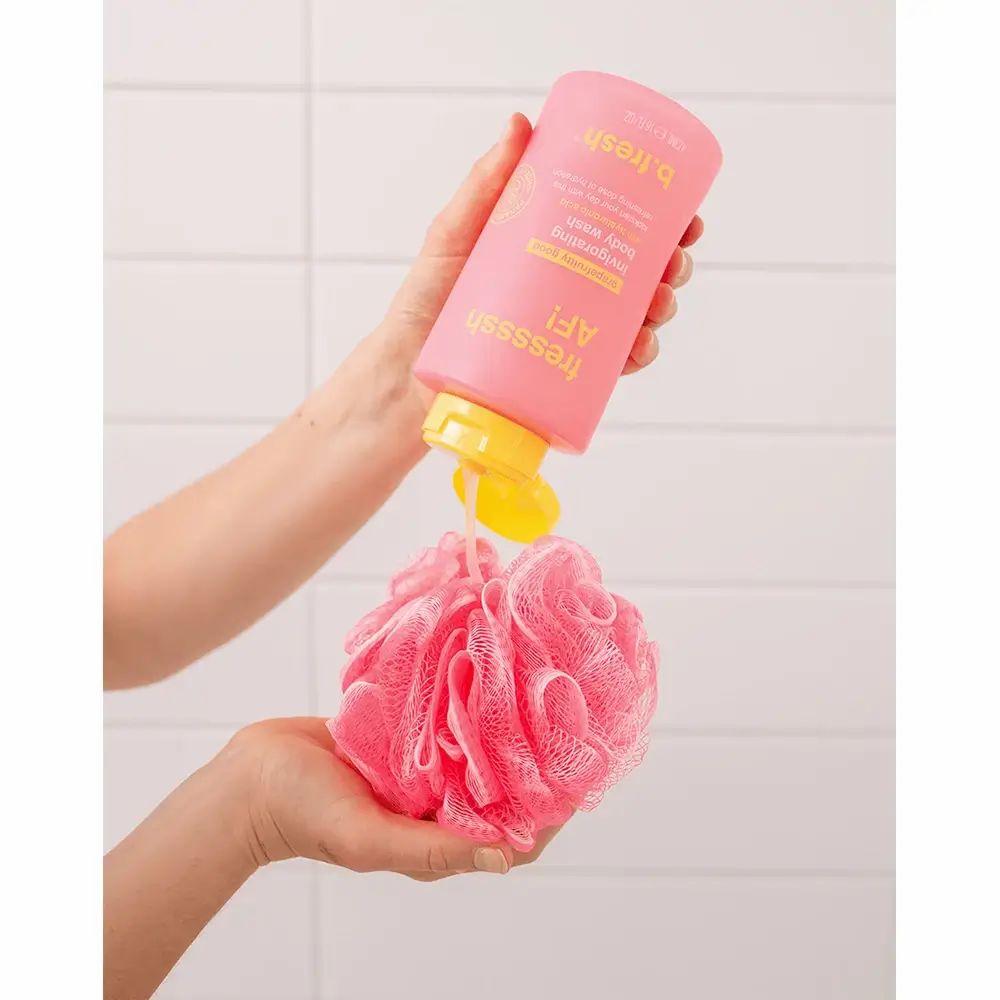 Flacone di gel doccia rosa versato su una spugna da bagno rosa. Tappo giallo. Mani che tengono il flacone e la spugna.