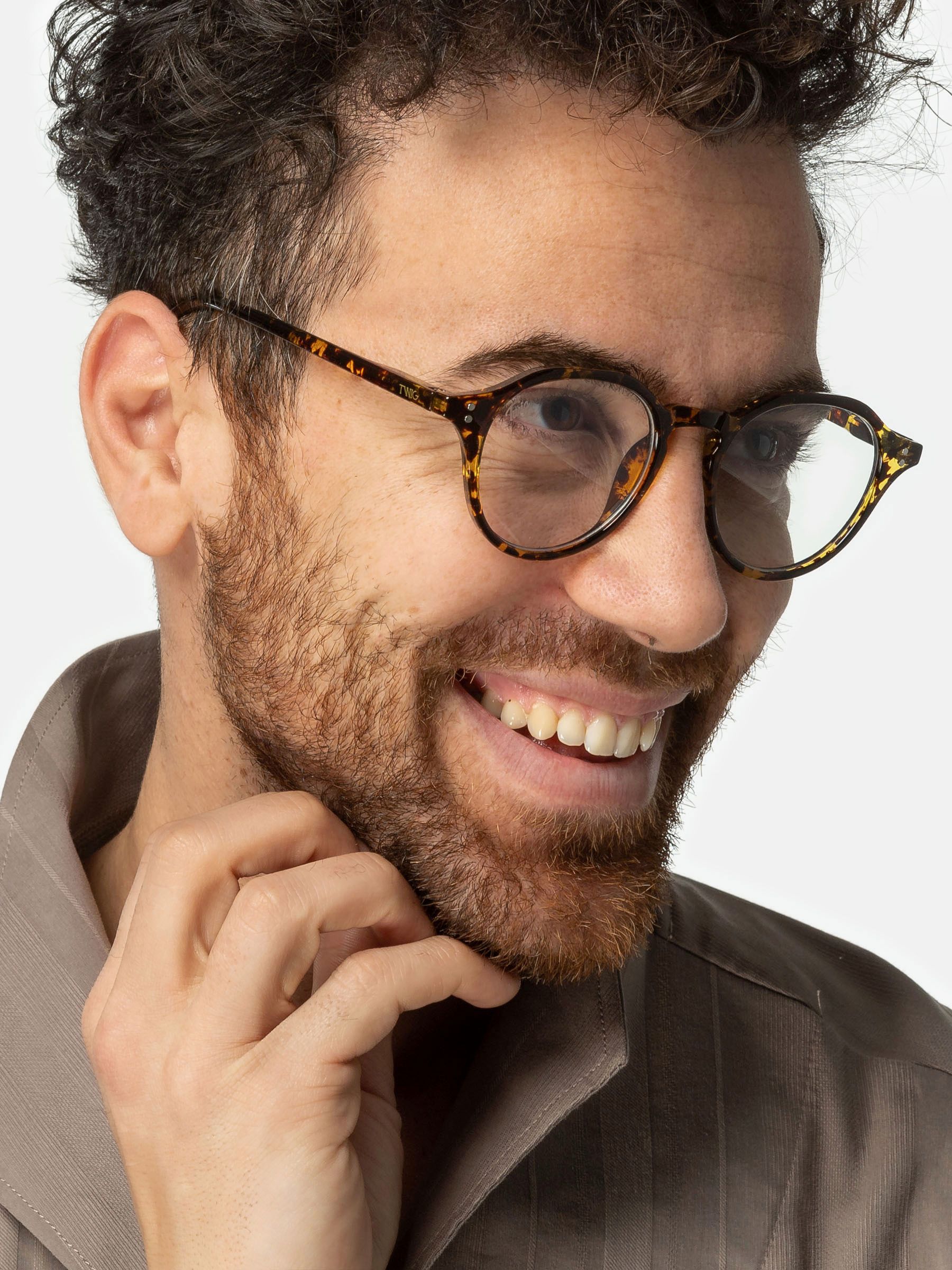 Uomo con occhiali. Lenti rotonde, motivo leopardato marrone. Sorride. Camicia beige.