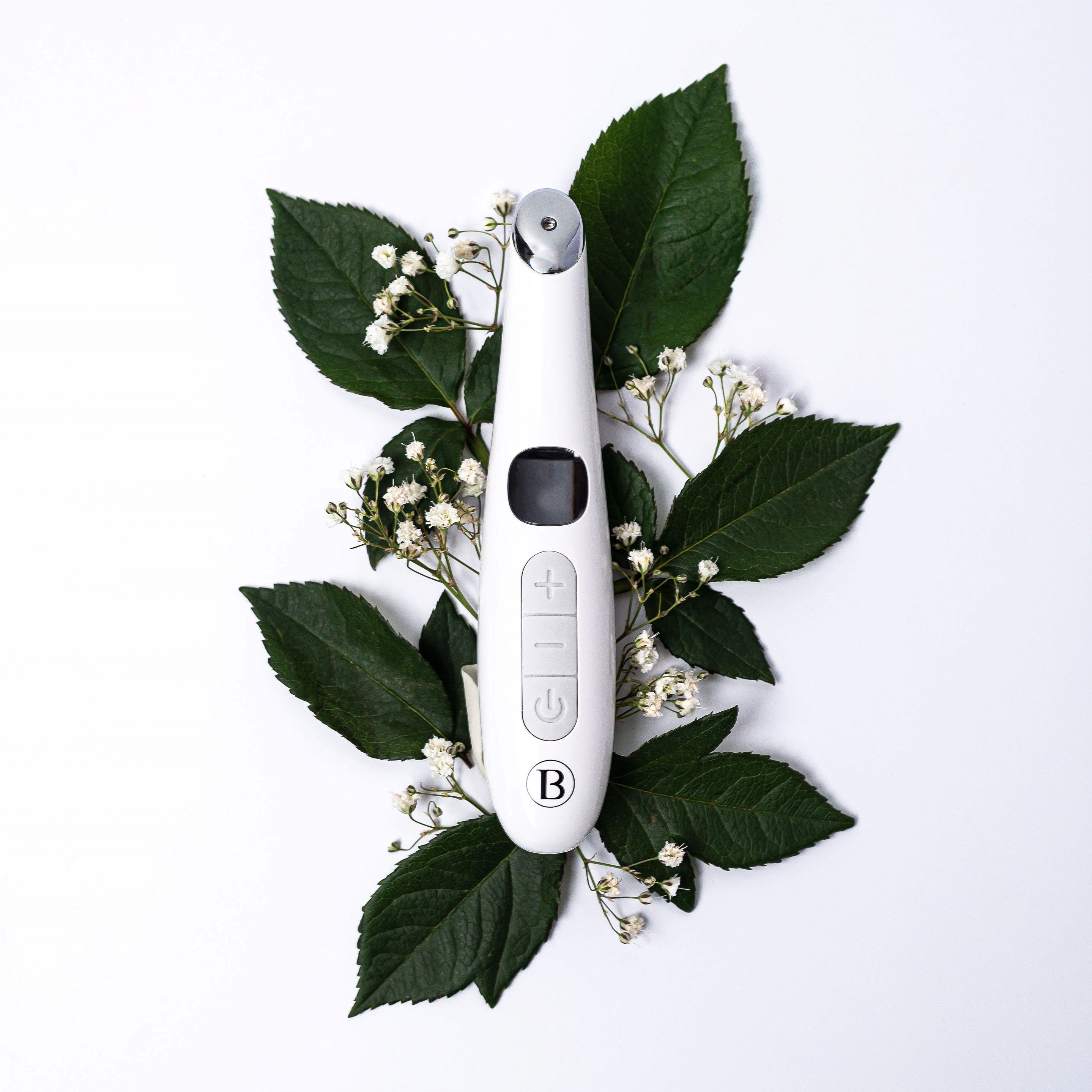 Dispositivo bianco con display, pulsanti e punta rossa. Circondato da foglie verdi e fiori bianchi.