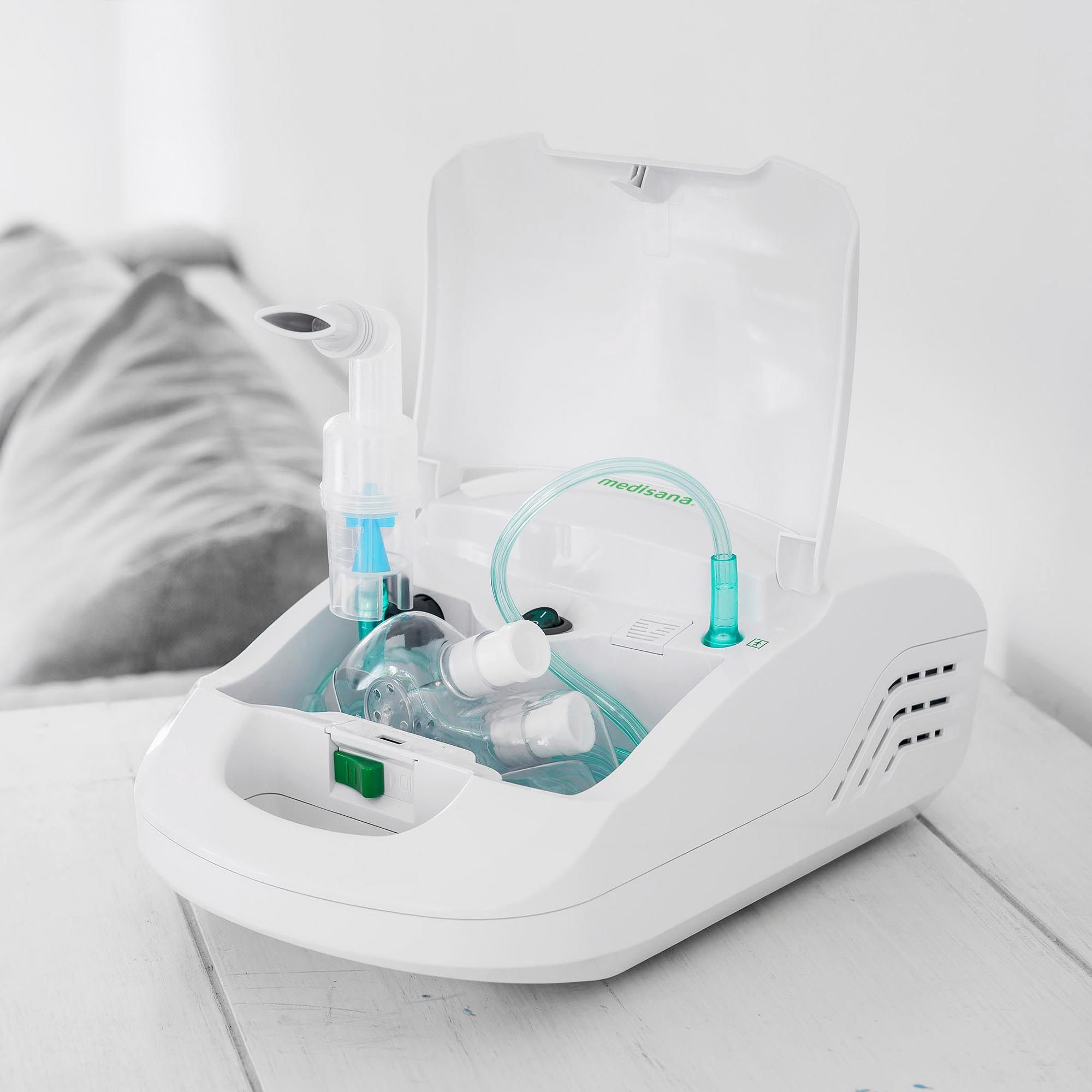 Inalatore bianco, aperto. Accessori all'interno. Dettagli verdi. Posizionato su un divano.