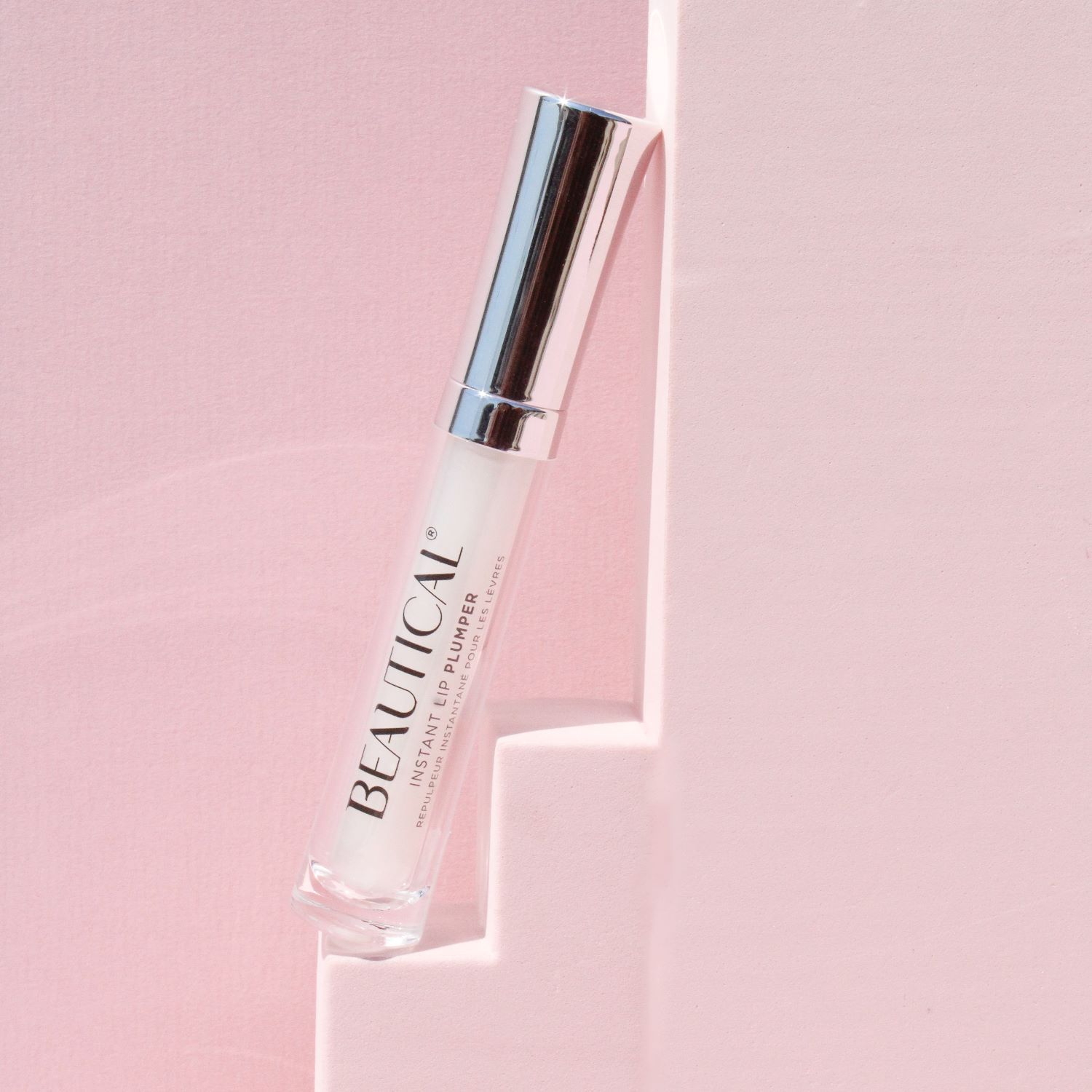 BEAUTICAL Instant Lip Plumper. Tubo con tappo argento, appoggiato a una parete rosa. Applicatore bianco.