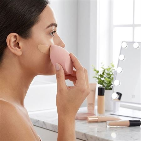 Una donna applica il fondotinta con una spugnetta rosa.