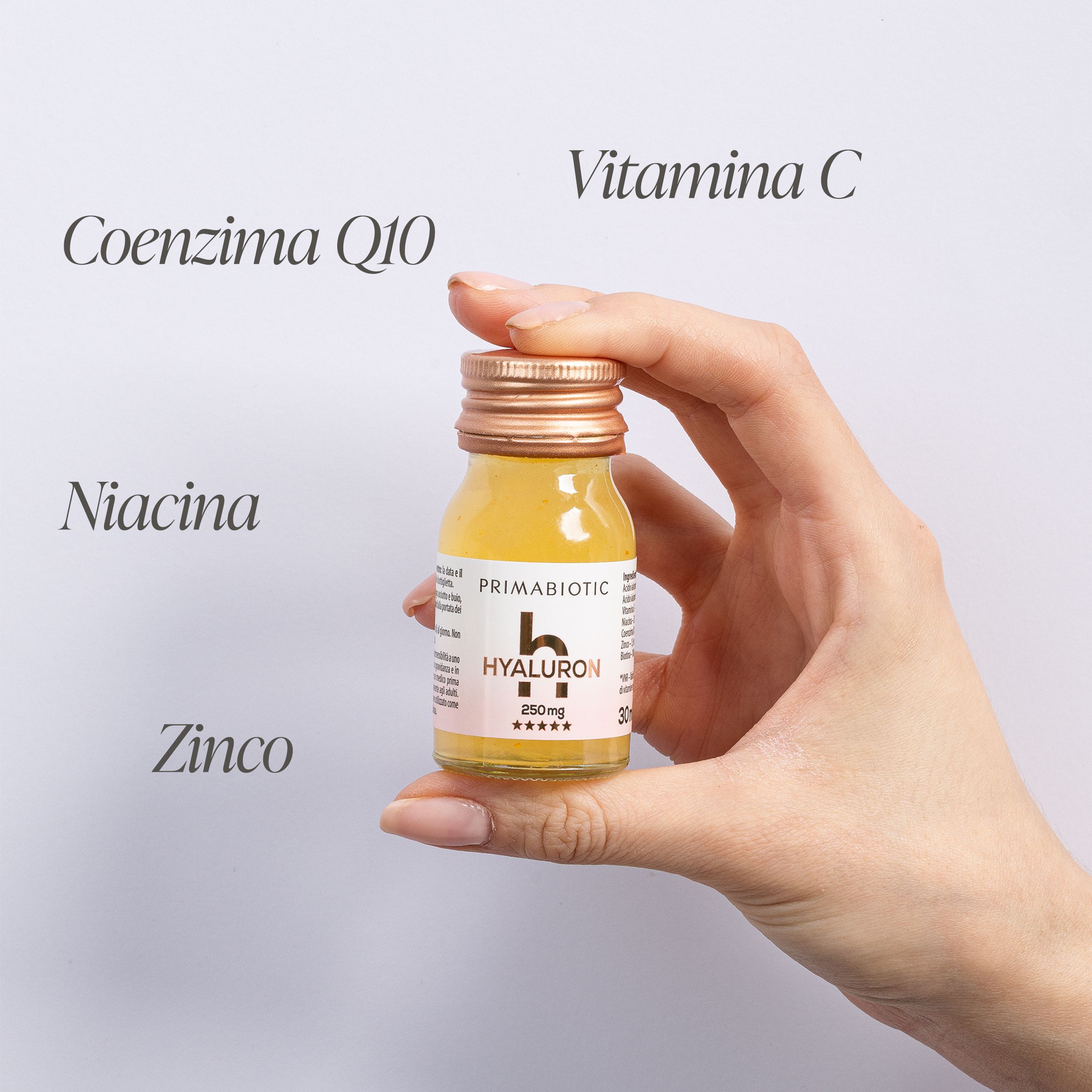 Primabiotic Hyaluron Shot: Mano che tiene una fiala, accanto Coenzima Q10, Niacina, Zinco, Vitamina C.
