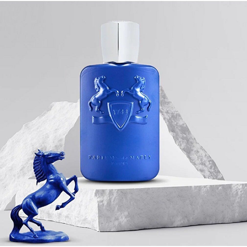 Flacone di profumo blu con tappo argentato. Stemma in rilievo sul flacone. Su piedistallo bianco.