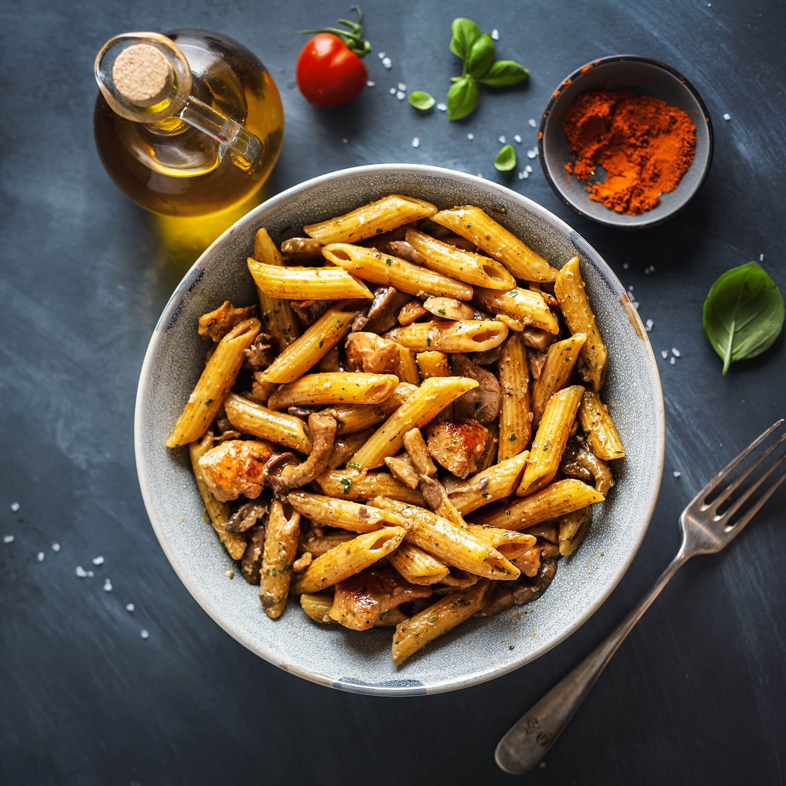 Ciotola di penne rigate con pollo e funghi. Guarnito con olio, pomodoro e spezie.