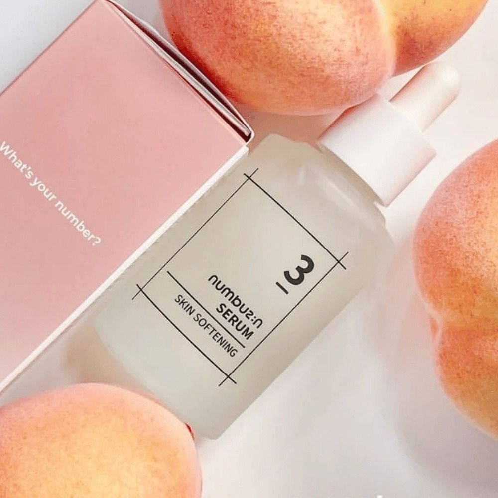 Flacone di siero con pesche e confezione. Scritta: 3, Serum, Skin Softening. Confezione rosa con testo: What's your number?