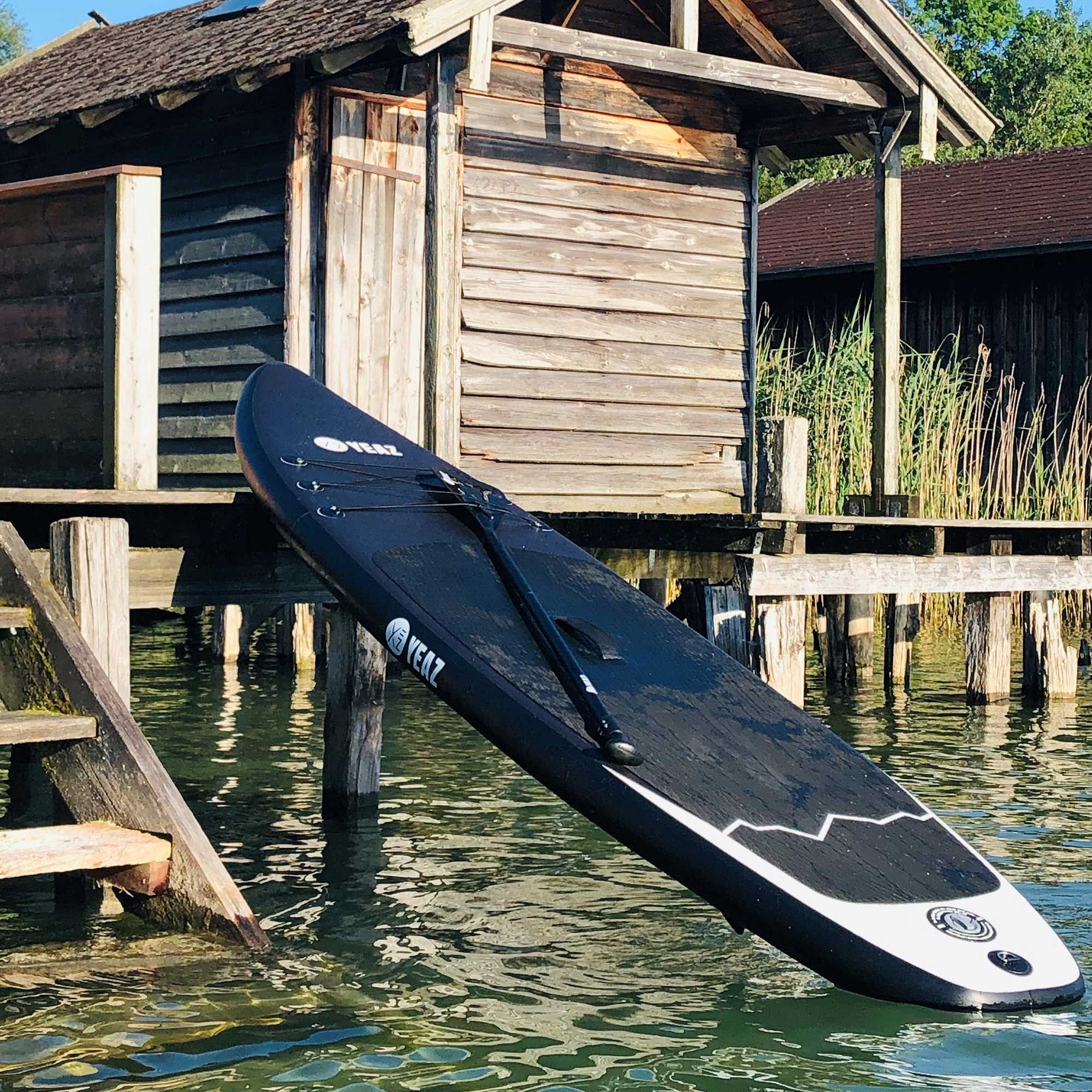 Tavola da paddleboard nera con design bianco e pagaia, appoggiata sull'acqua.