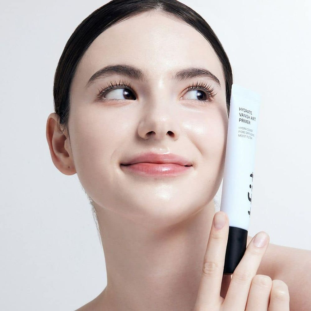 Donna tiene tubo con HYDRATE VANISH ART PRIMER. Testo: HYDRA COVER, PORE DIFFUSING, MOIST FILTER.