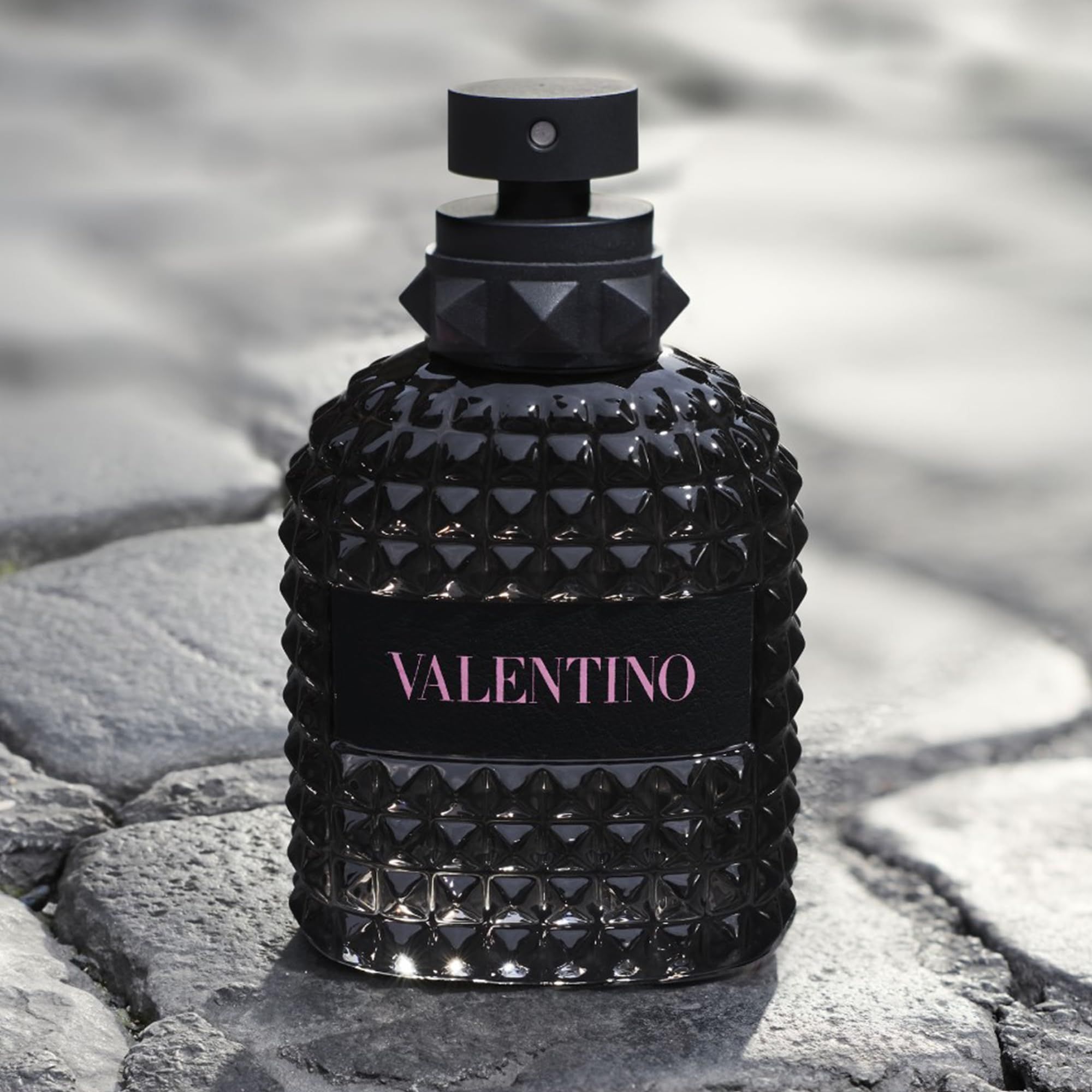 Flacone Valentino nero su pavimento in pietra. Flacone con motivo e tappo nero.