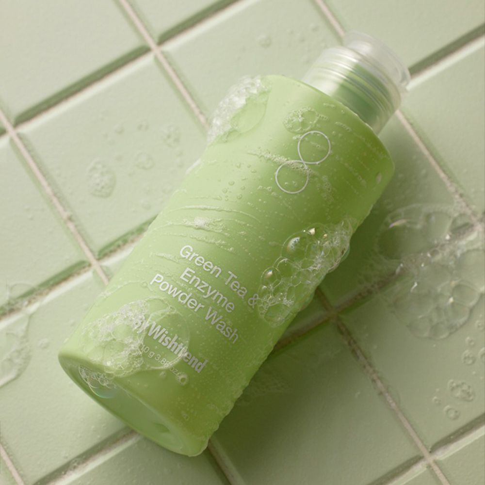 Flacone verde con schiuma su piastrelle verdi. Scritta: Green Tea & Enzyme Powder Wash. Marchio: By Wishtrend.