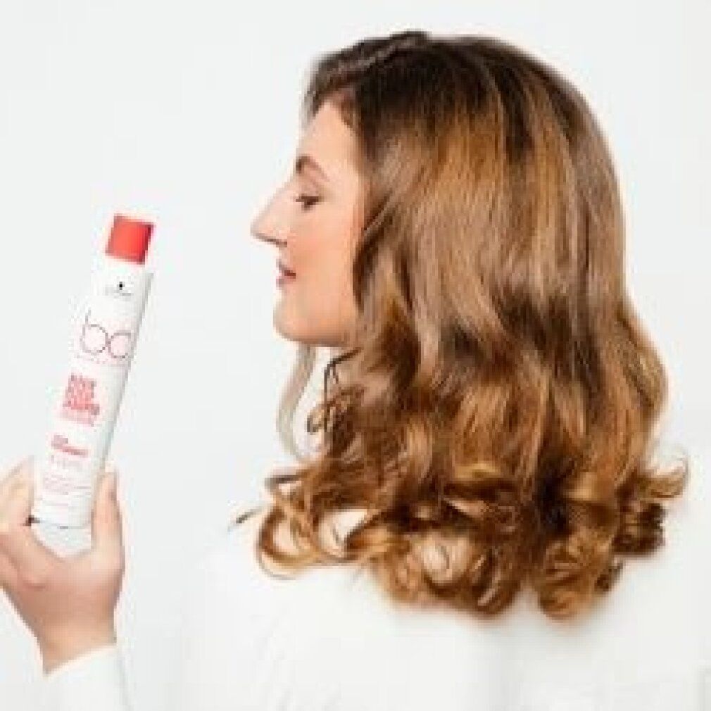 Donna tiene un flacone. Scritta: bc Bonacure Repair Rescue Conditioner Arginine. Donna di profilo, capelli mossi.