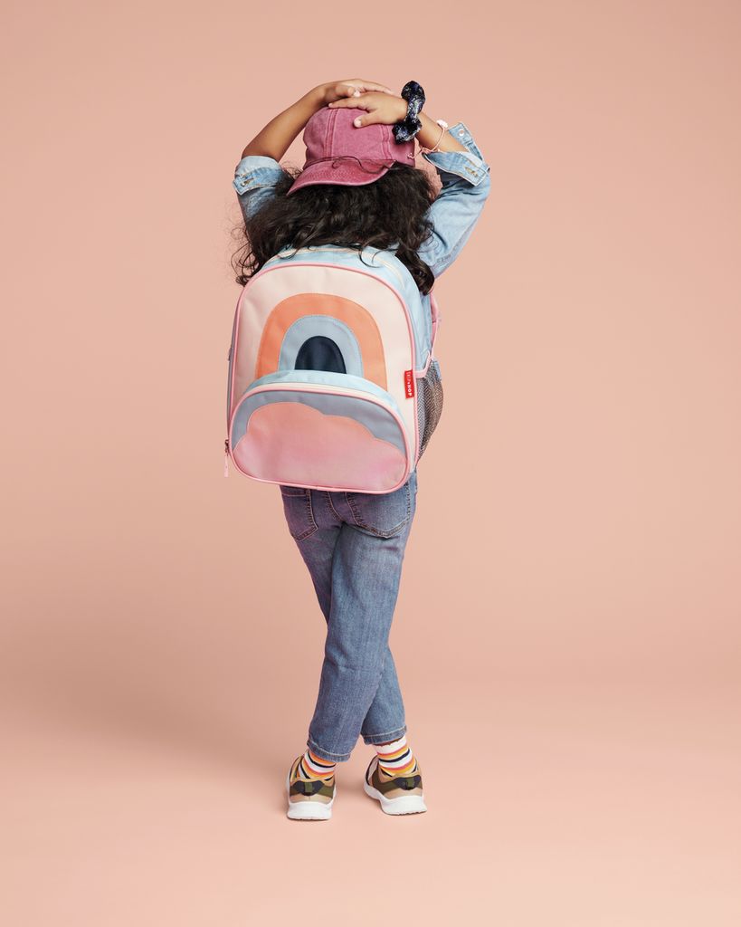 Bambino con zaino, design arcobaleno. Elementi rosa, blu e arancioni. Il bambino indossa jeans, giacca e cappello. Vista posteriore.