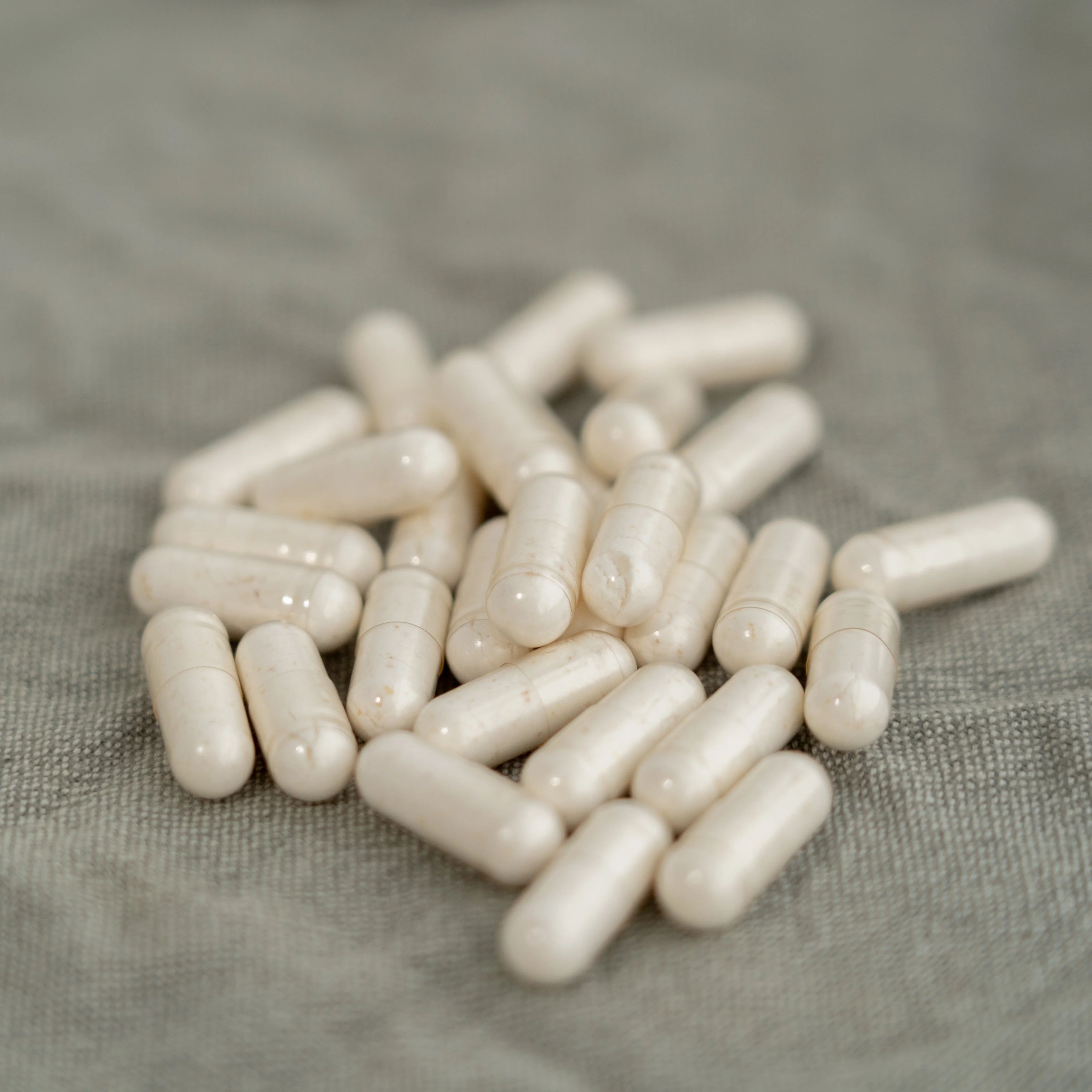 Mucchio di capsule bianche. Capsule oblunghe, traslucide, su una superficie grigia.