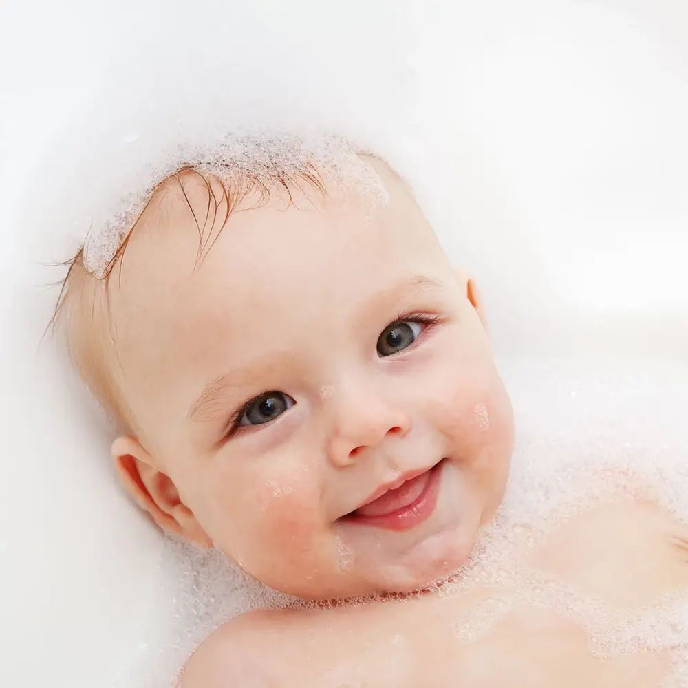 Viso di bambino nella schiuma di sapone. Sorriso, occhi aperti.