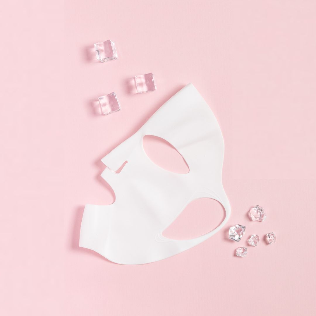 Maschera in silicone bianca su sfondo rosa. Cubetti di ghiaccio accanto. Maschera con aperture per occhi e bocca.