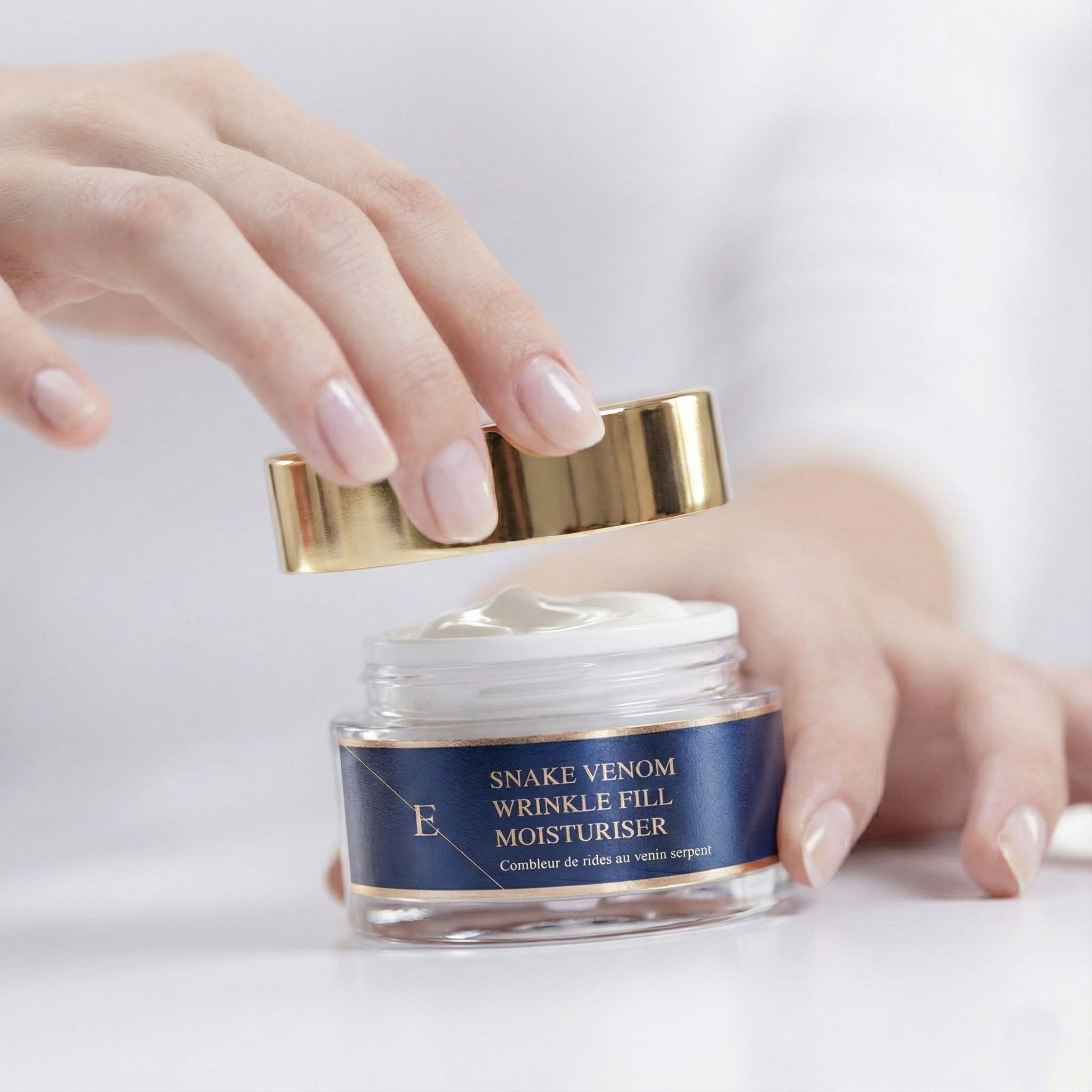 Mani che aprono un vasetto di crema. Scritta: Snake Venom Wrinkle Fill Moisturiser. Coperchio dorato.