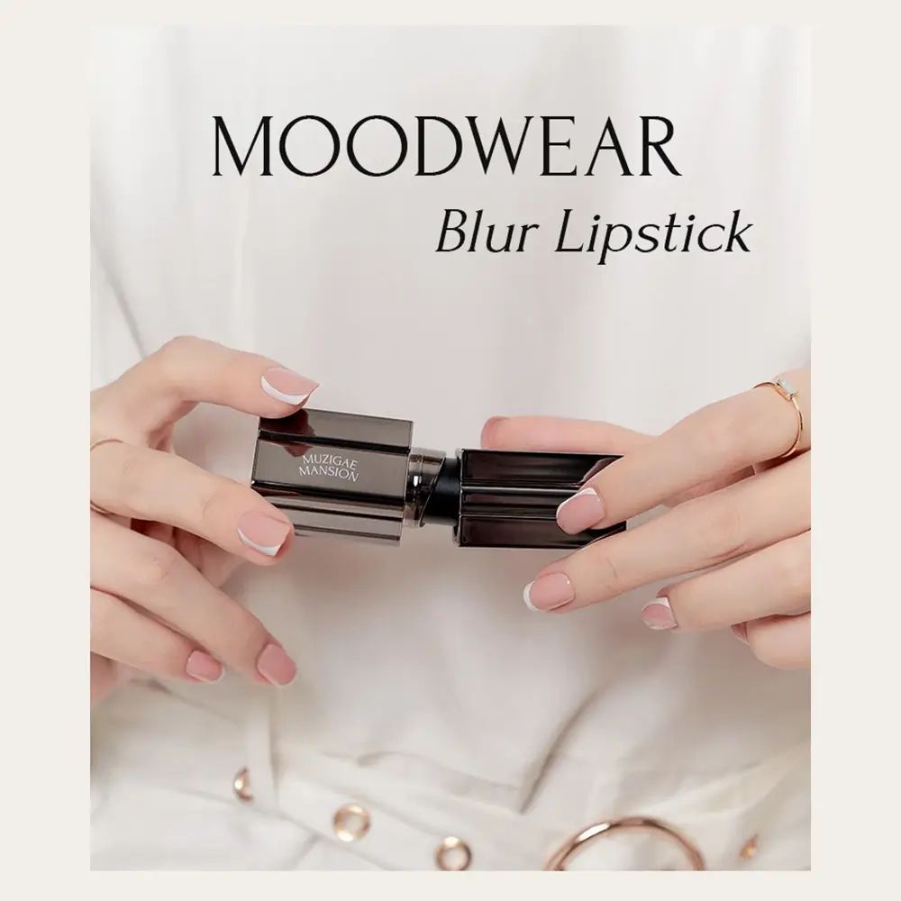 Mani che tengono un rossetto. Testo: MOODWEAR Blur Lipstick. Custodia argentata, cappuccio nero.