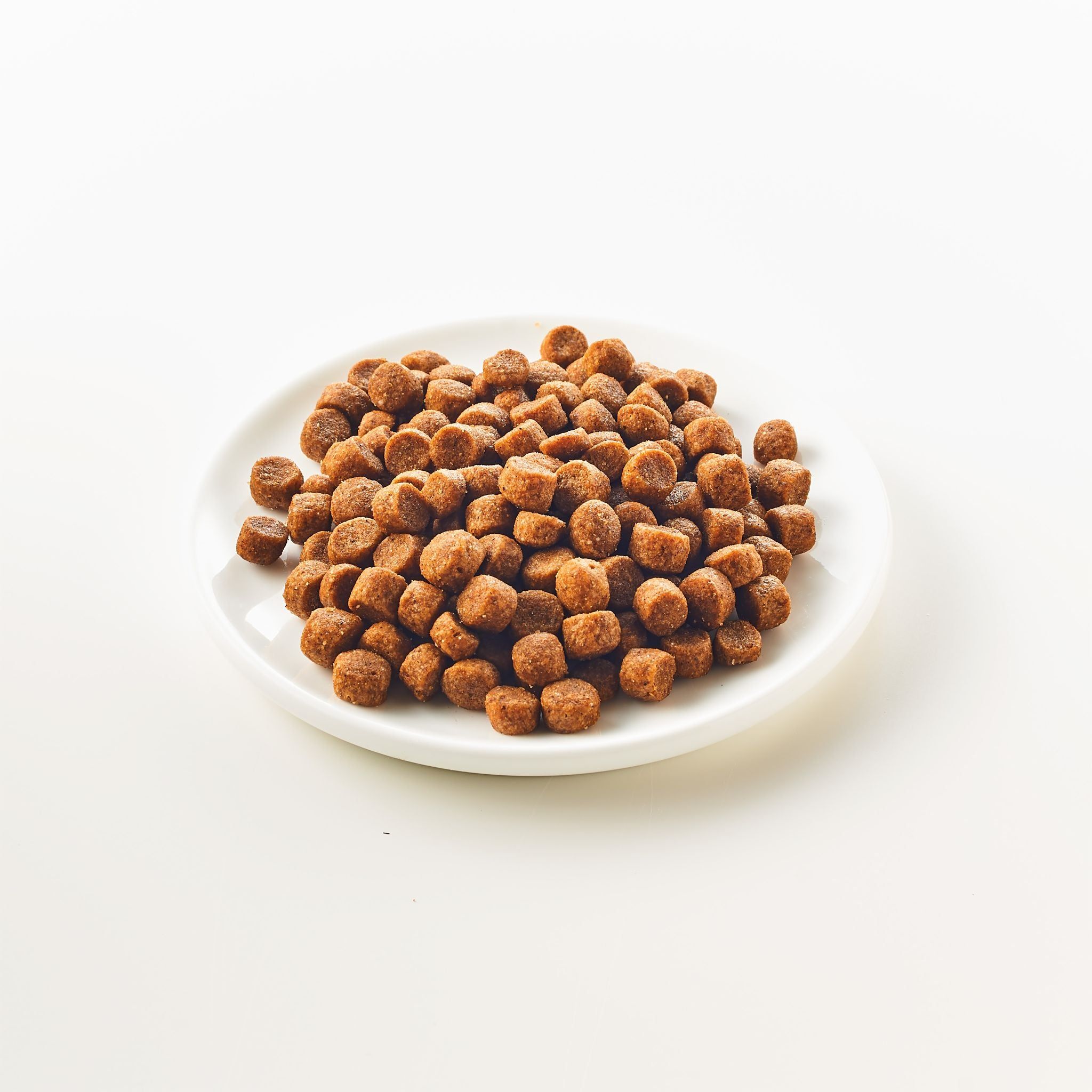 Mucchio di crocchette quadrate marroni su piatto bianco. Su sfondo chiaro.