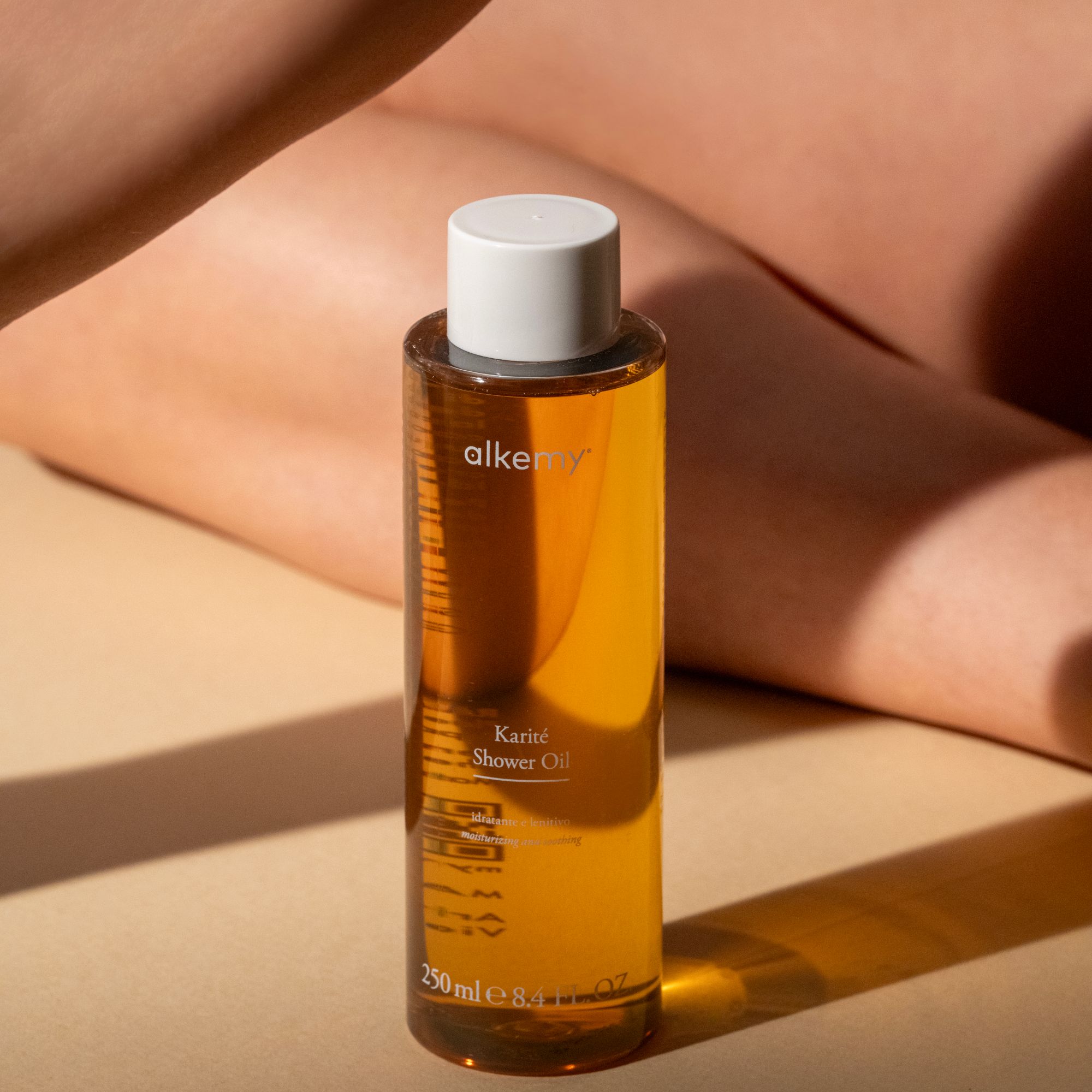 Una bottiglia di olio doccia Alkemy Karité davanti a una persona.