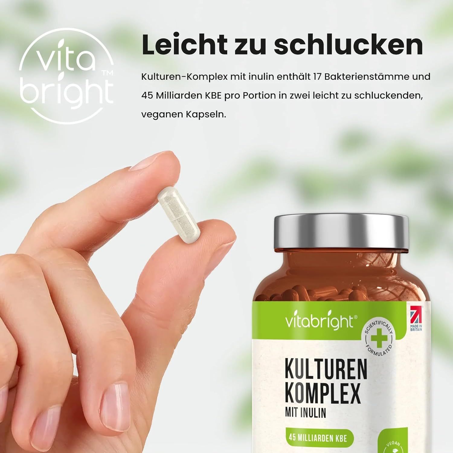 Mano che tiene una capsula di VitaBright Kulturkomplex. Flacone marrone sullo sfondo. Contiene 17 ceppi batterici e inulina.
