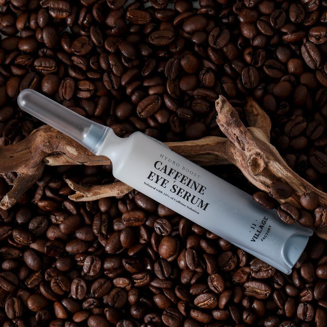 Flacone del prodotto su chicchi di caffè. Testo: Hydro Boost Caffeine Eye Serum. Contiene il 10% di caffeina. Pezzo di legno sullo sfondo.