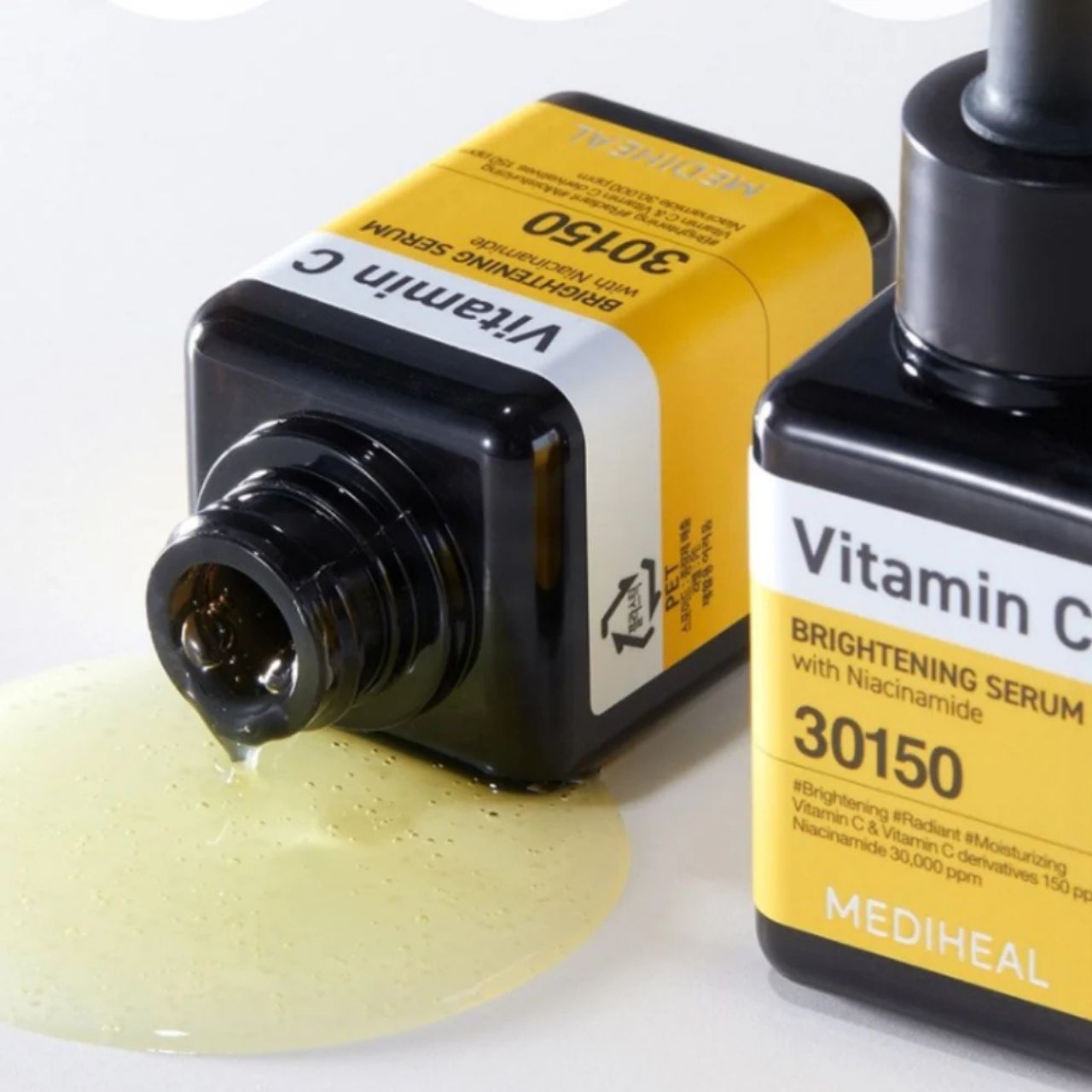 Due flaconi di siero Mediheal Vitamina C, uno rovesciato con siero che fuoriesce. Etichette gialle con scritte nere.