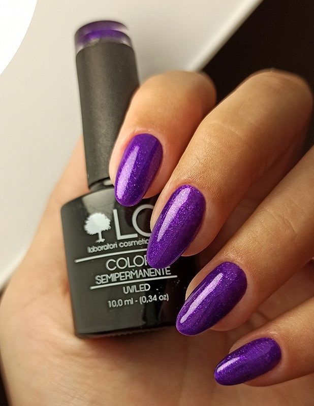 Mano con unghie smaltate e flacone di smalto. Unghie e flacone viola glitter. Scritta: LCI, COLORE SEMIPERMANENTE.