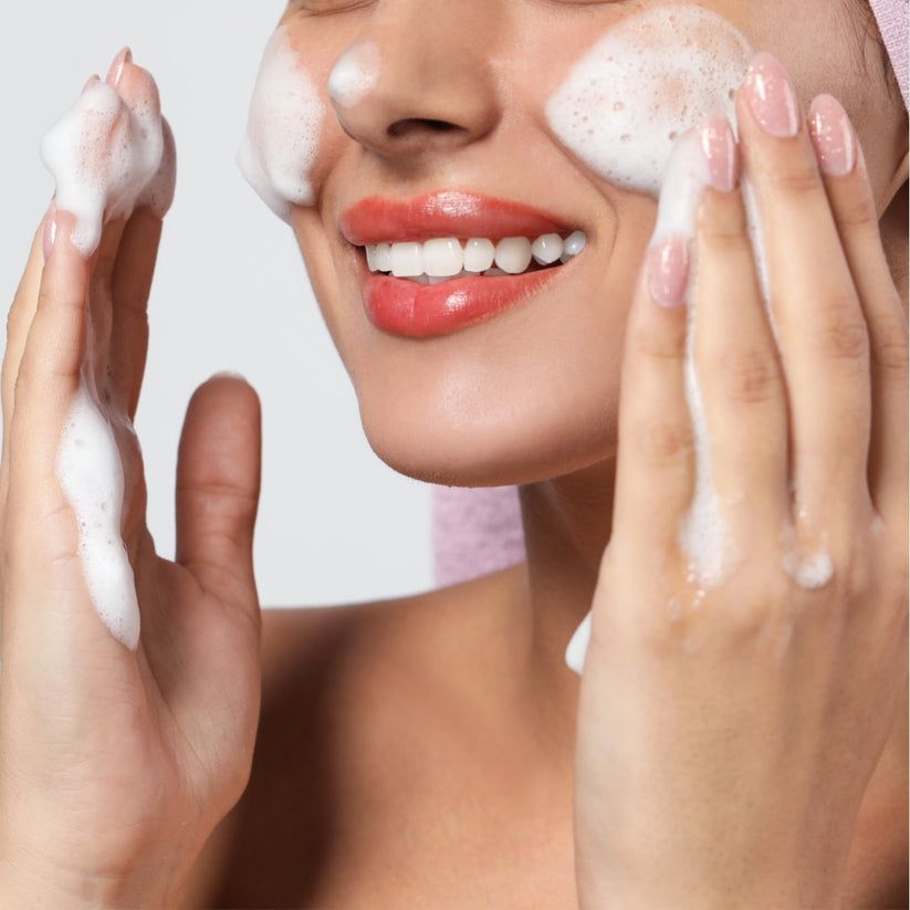 Primo piano di una persona che si lava il viso con la schiuma. Mani coperte di schiuma. Sorriso.