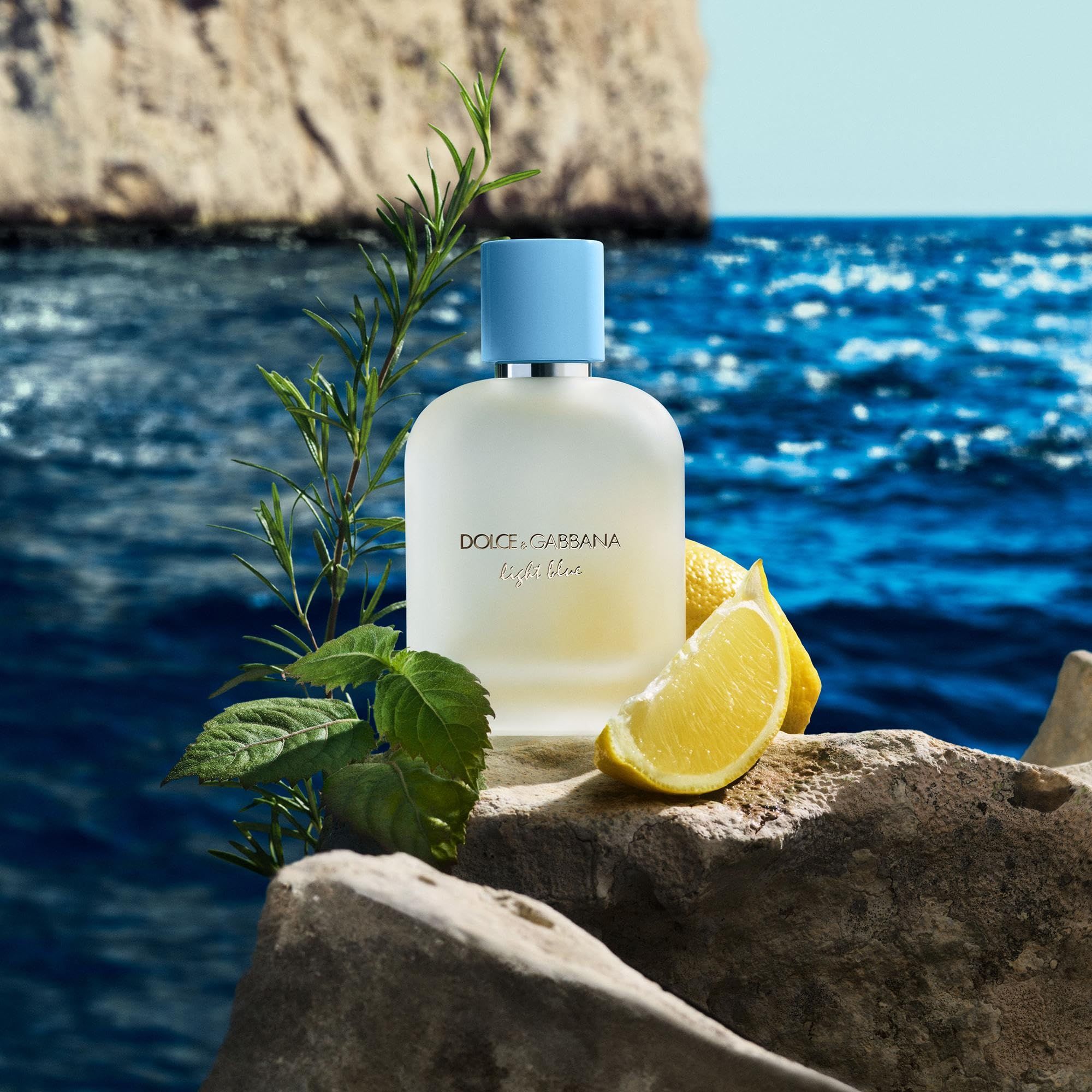 Flacone di profumo su una roccia, circondato da piante e limoni. Scritta: Dolce & Gabbana Light Blue. Tappo azzurro chiaro.