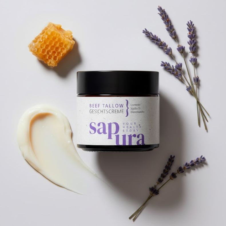 Vasetto di crema, favo, rametti di lavanda e macchia di crema. Scritta: BEEF TALLOW GESICHTSCREME. Marchio: sapura.