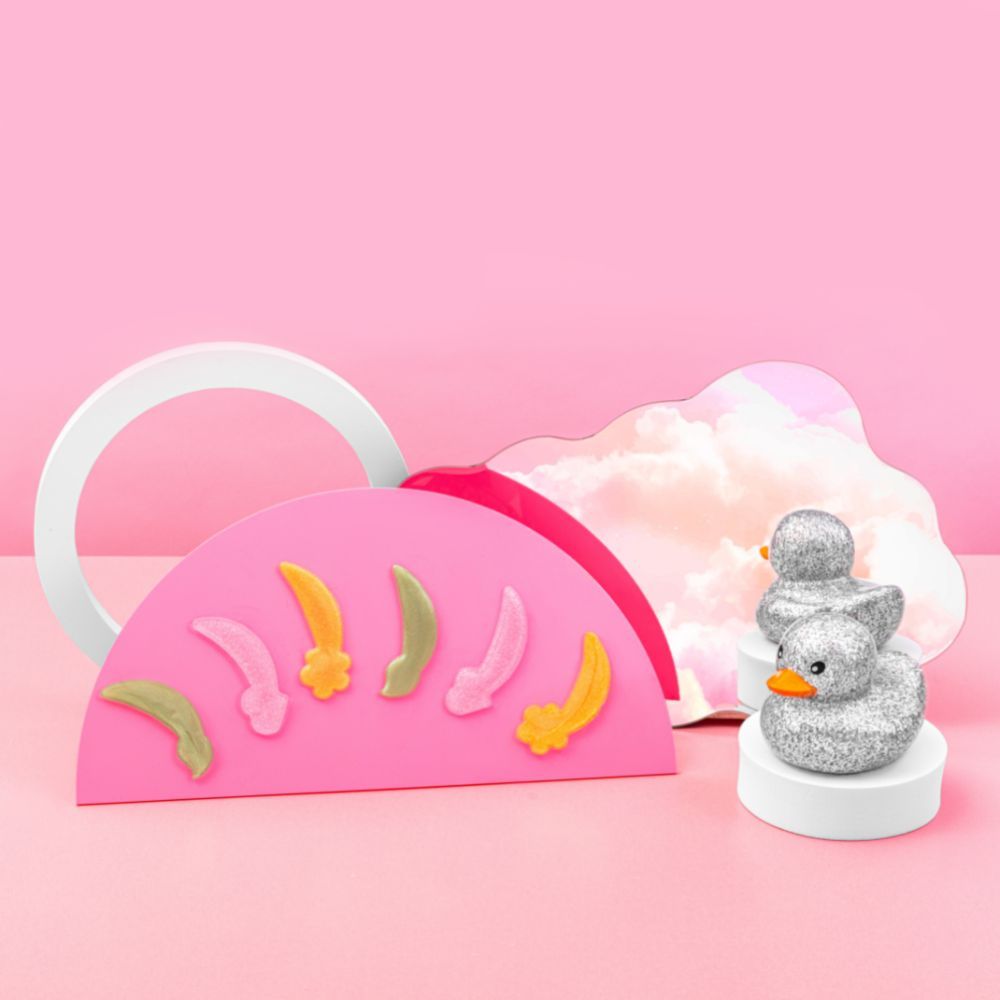 Sfondo rosa con elementi decorativi. Oggetto a forma di mezza luna con patch per occhi. Anatra glitterata.